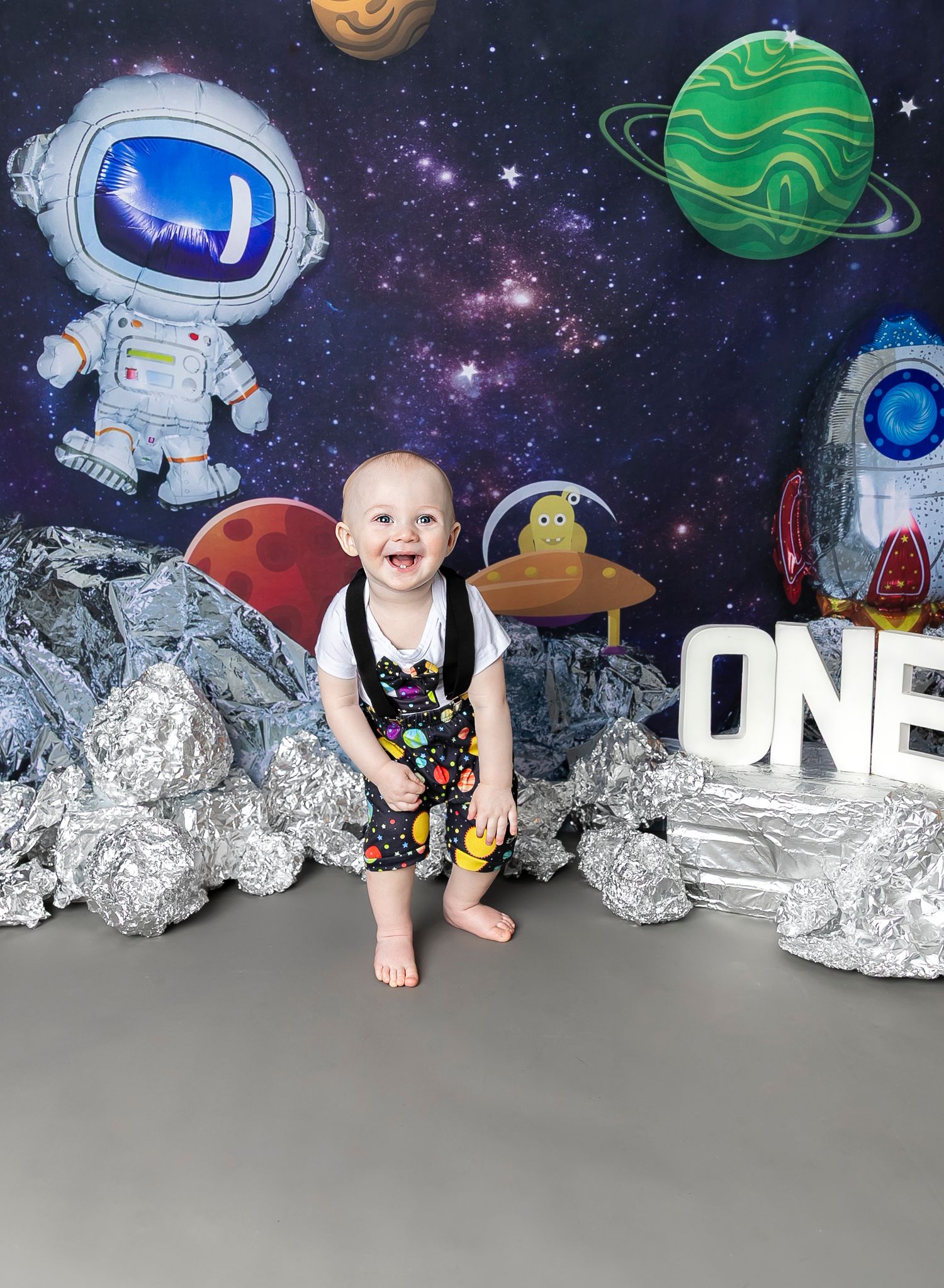 Space-themed first birthday photo setup with a starry backdrop, astronaut, planets, and moon rock decorations in Pittsburg KS and Joplin MO.