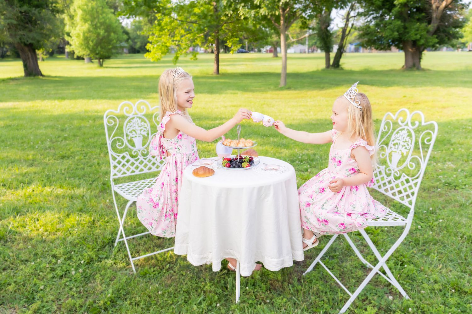 Two children in pink dresses enjoy an elegant outdoor tea party during a princess mini session photoshoot in Pittsburg KS and Joplin MO.