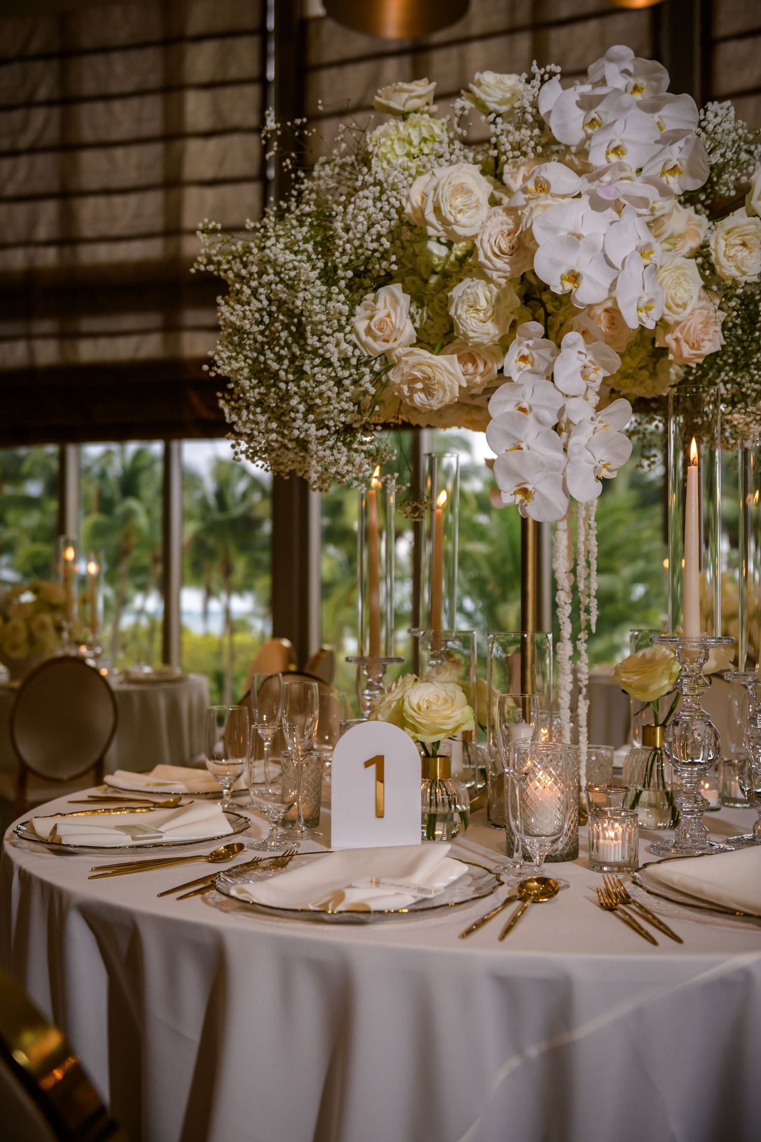 Elegant wedding table setting with tall white floral centerpiece and gold accents.