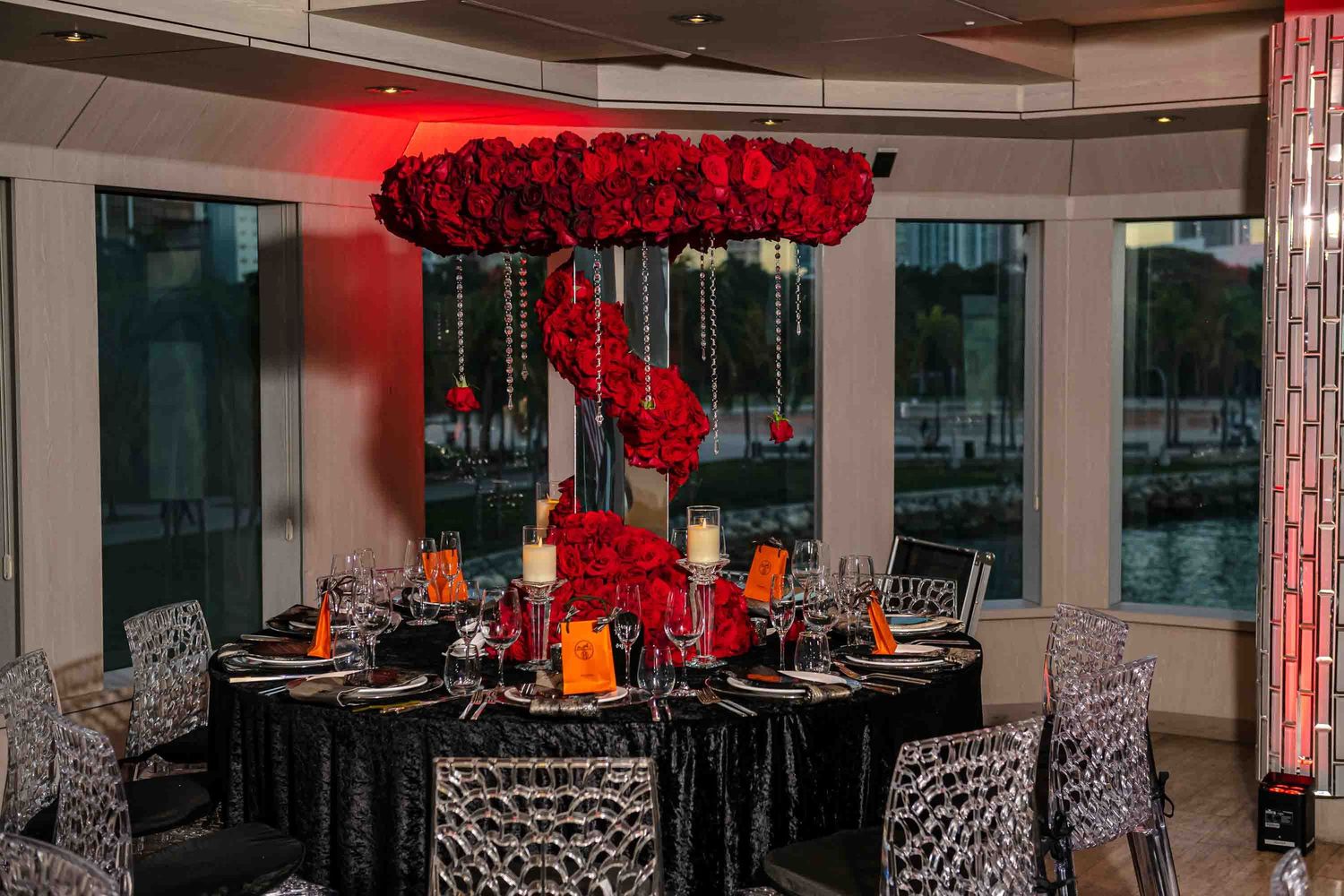 Modern reception table with suspended red floral arrangement and black sequin linens in waterfront venue on the Seafair Mega Yacht in Miami.