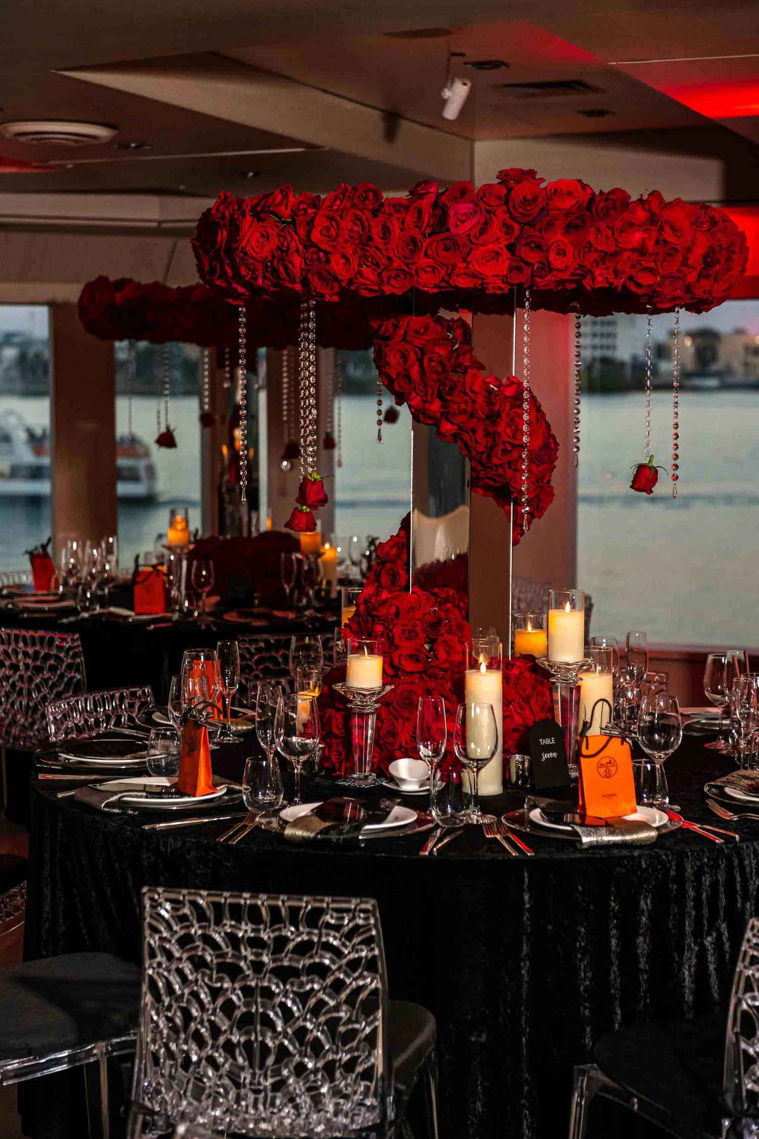 Dramatic dining setup with hanging red rose centerpiece, black tables, and glowing candles on the Seafair Mega Yacht in Miami.