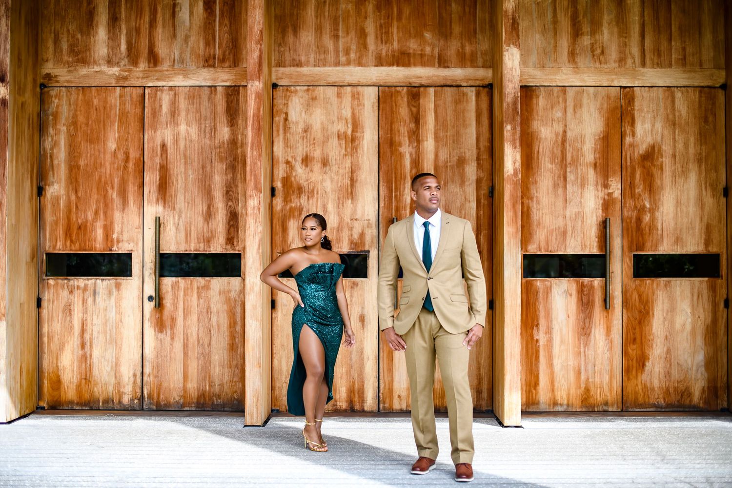 Stylish couple posing against rustic wooden doors in formal attire.