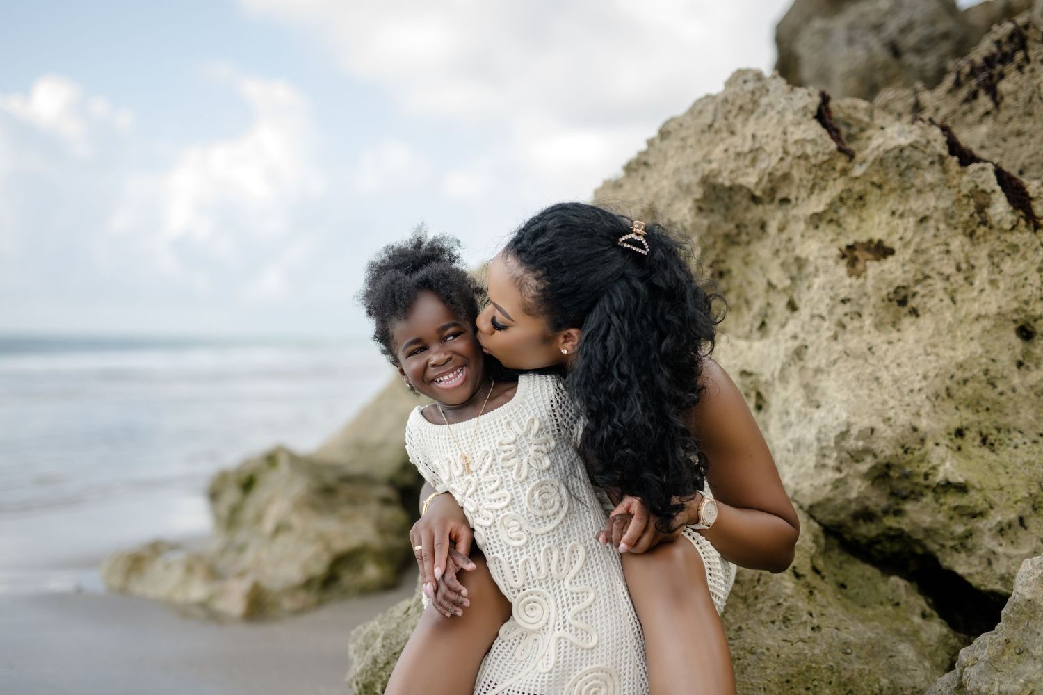 Two people in white outfits share a joyful embrace on a tropical beach.