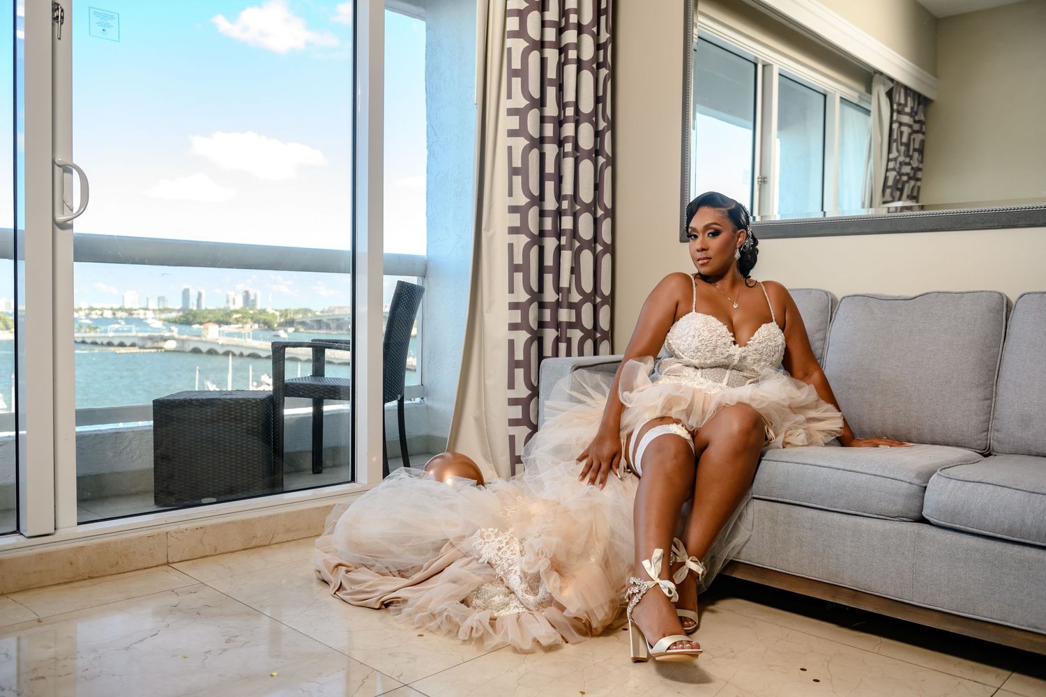 Woman in white dress relaxes on grey couch with waterfront view.