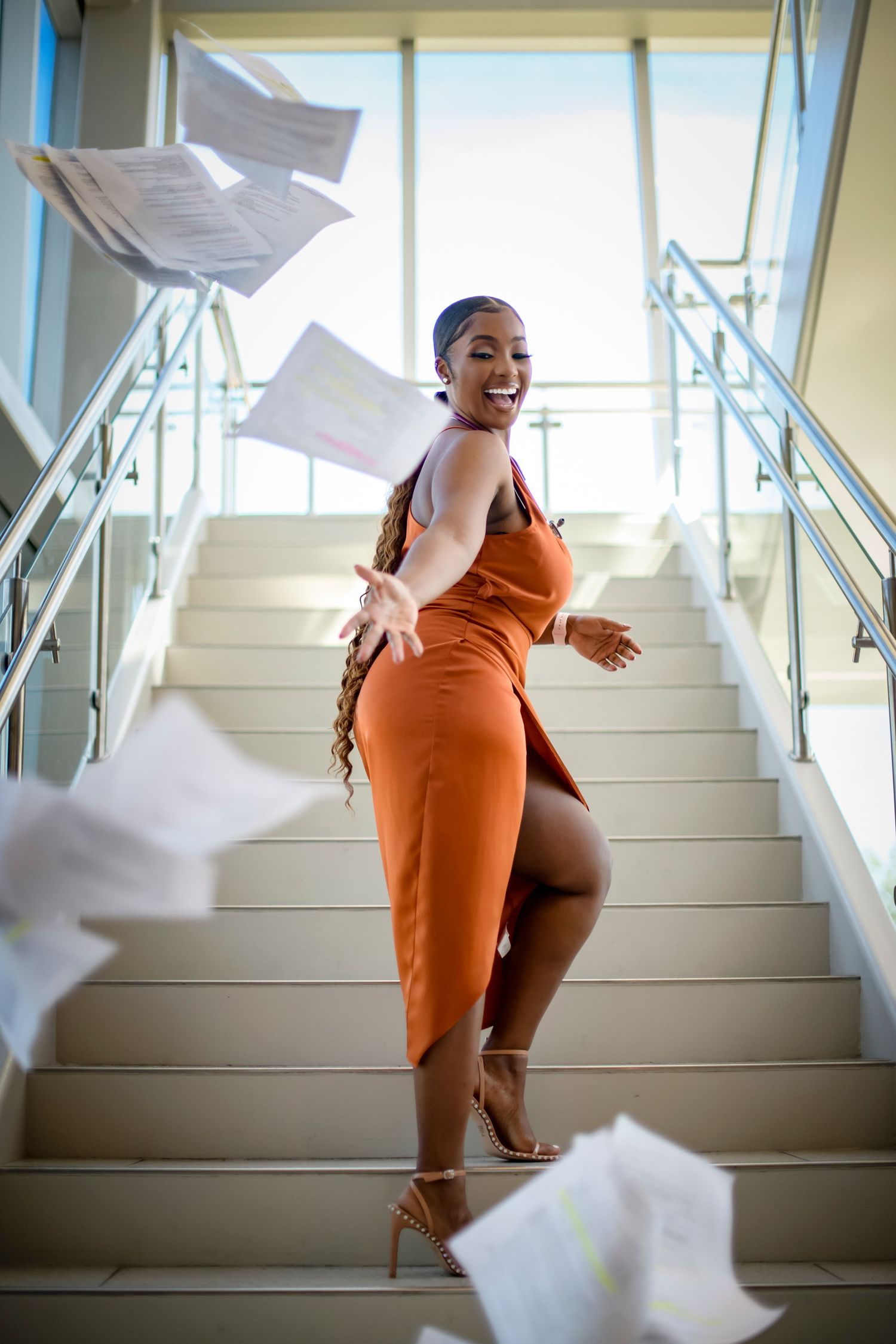 Figure in orange dress ascends white stairs as papers dramatically float and scatter through the air in sequence.