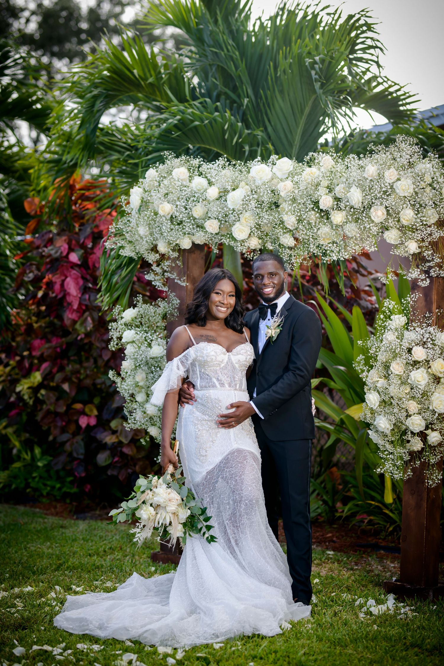 Beautiful wedding celebration in a lush tropical garden setting with white floral arch and elegant decor.