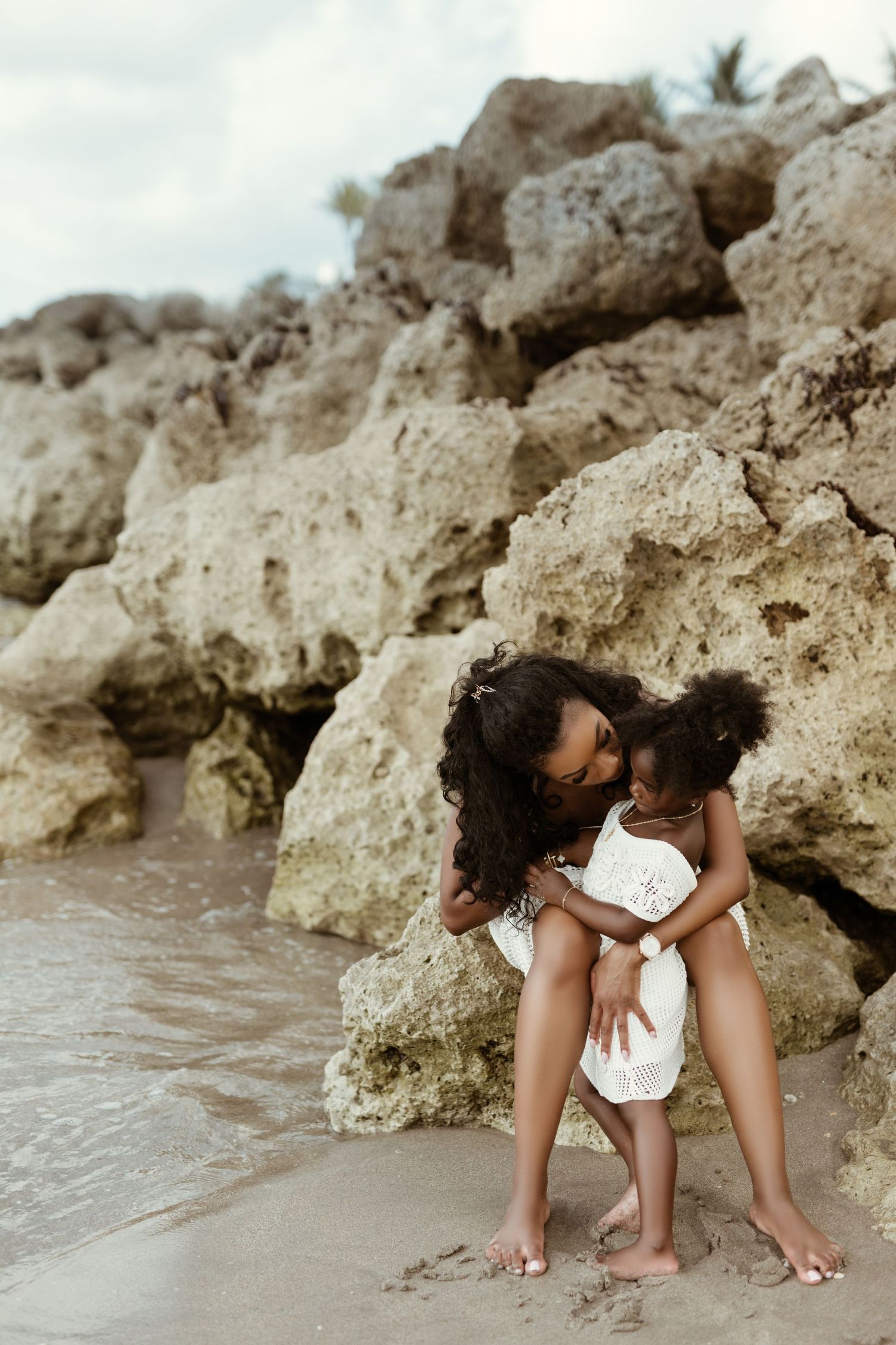 Tender moment between mother and child playing on beach near rocky shore.