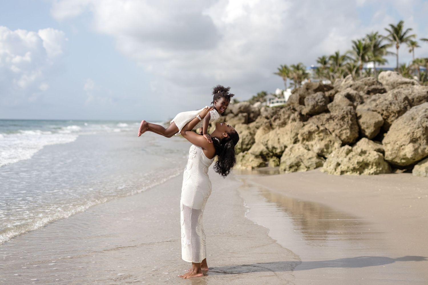 Two people in white clothing share a playful moment on a tropical beach.