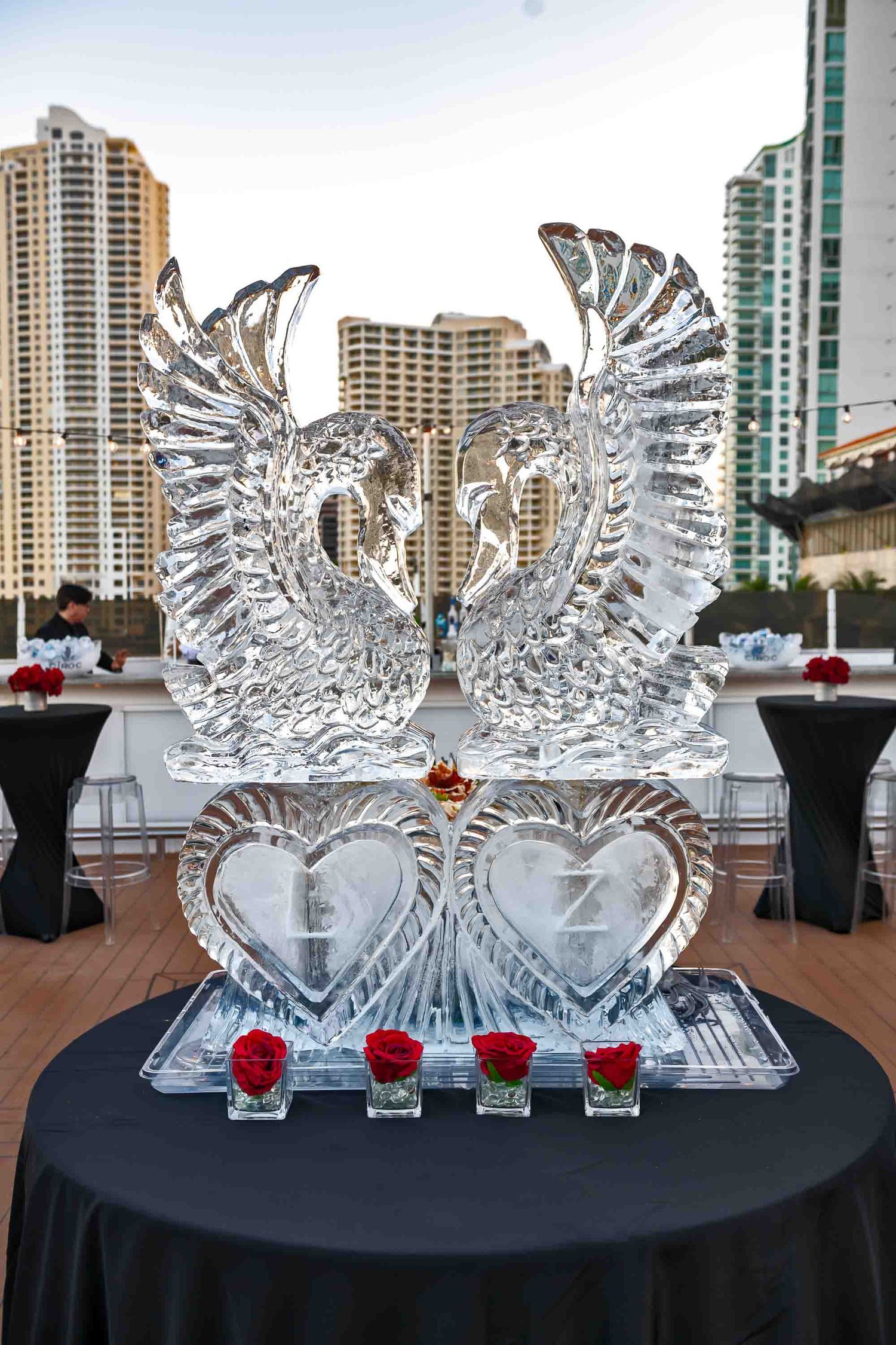 Crystal swan ice sculpture with heart designs displayed on black tablecloth with city buildings in background on the Seafair Mega Yacht.