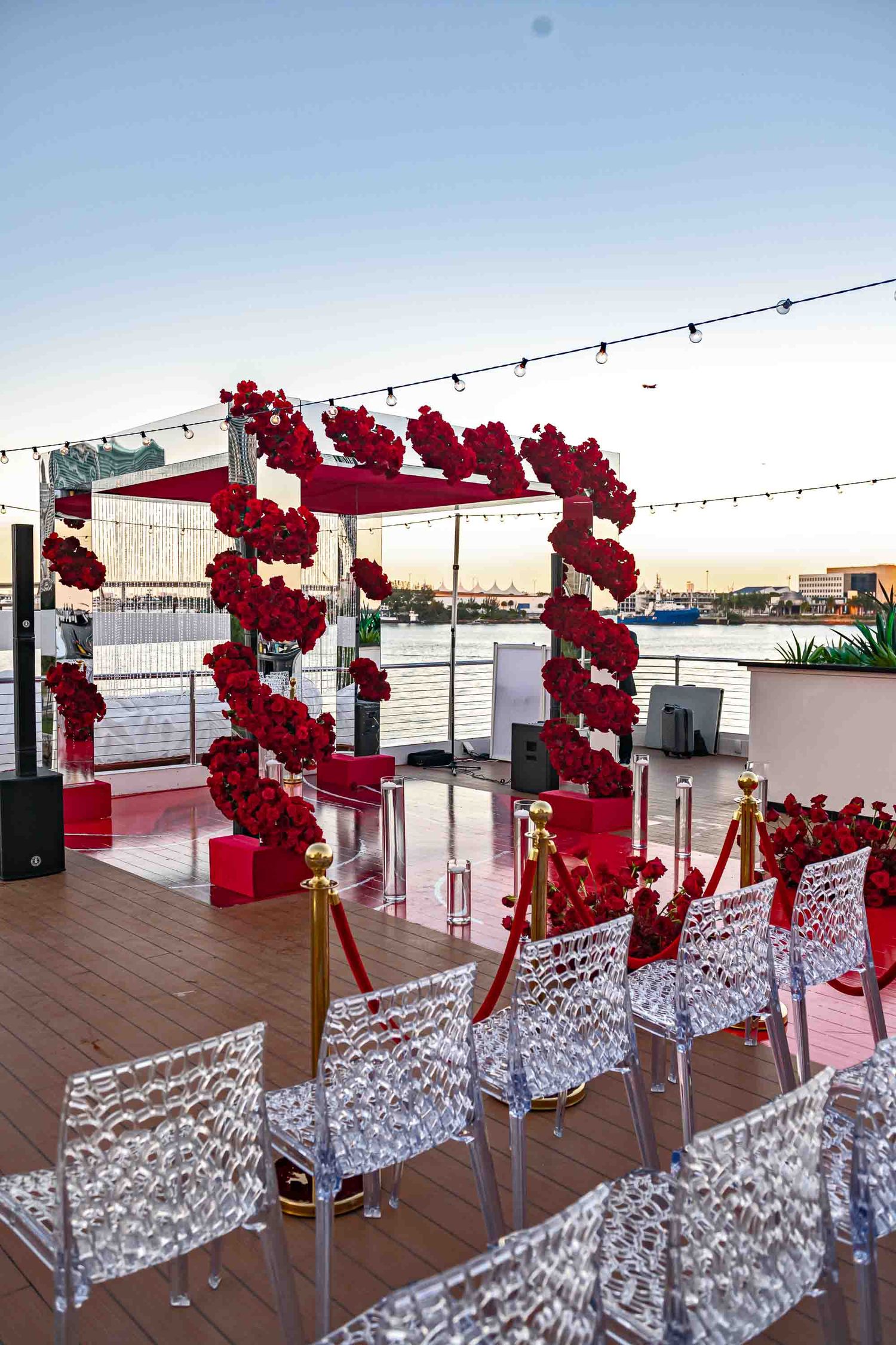 Wedding ceremony setup with red floral arch and transparent ghost chairs on waterfront deck on the Seafair Mega Yacht in Miami.