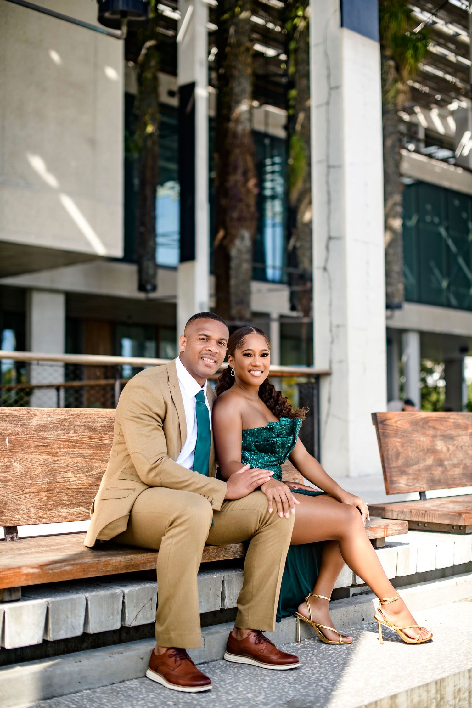 Well-dressed couple sitting together on wooden bench in urban setting.