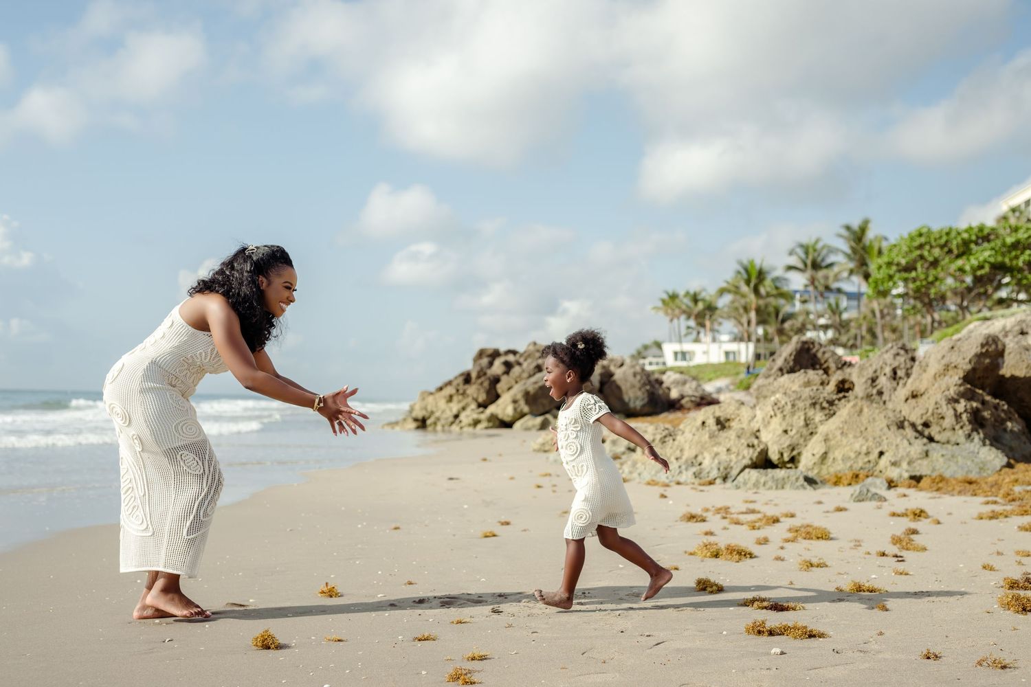 Two people in white dresses play chase on a tropical beach.