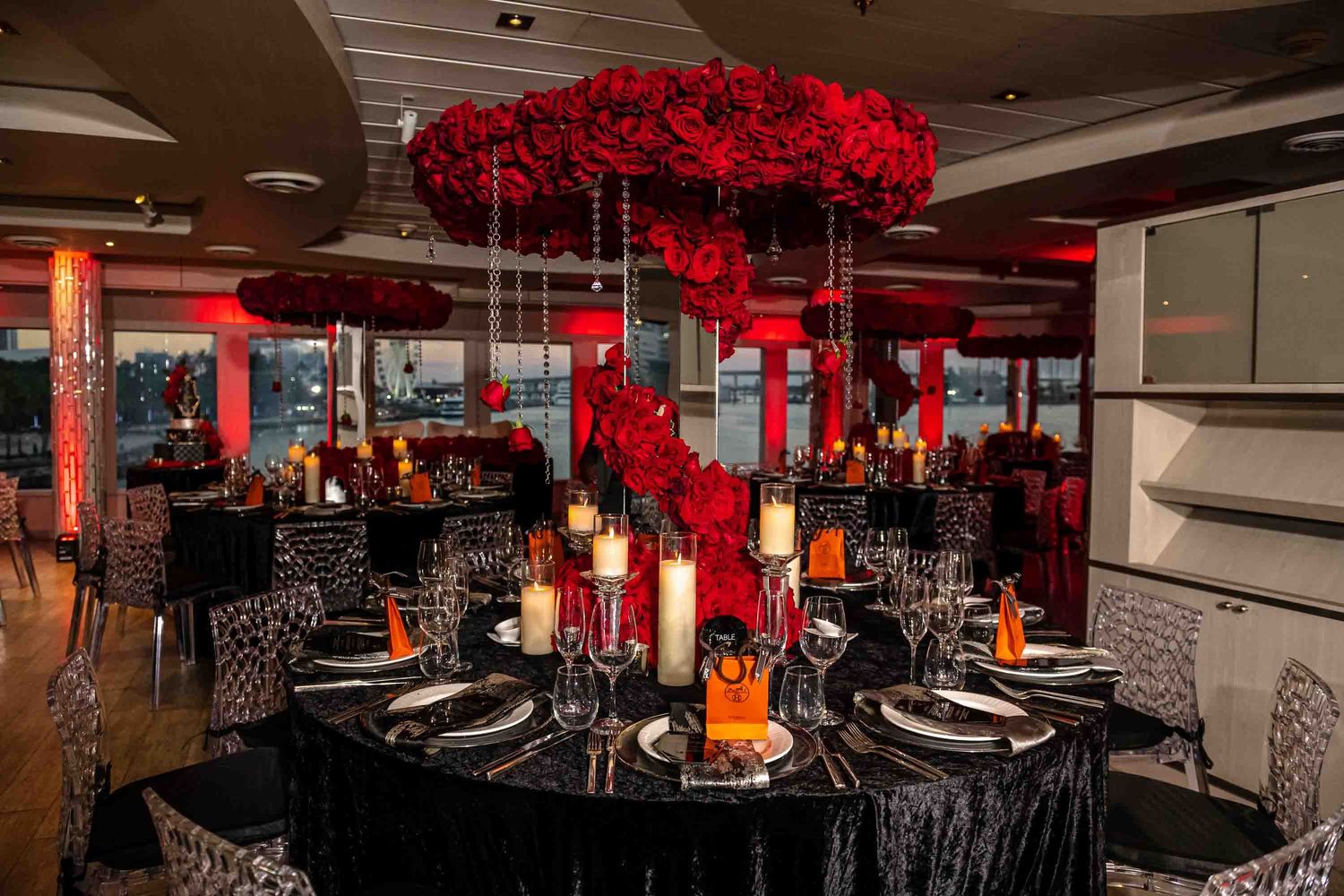 Sophisticated reception venue with red rose suspended centerpieces and candlelit black table settings on the Seafair Mega Yacht in Miami.