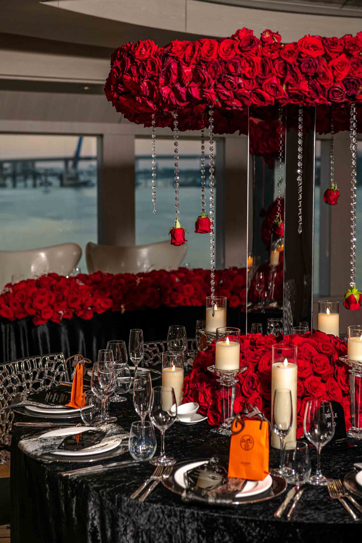 Elegant table setting with red rose centerpiece, crystal glassware, and hanging candles on black tablecloth on the Seafair Mega Yacht,