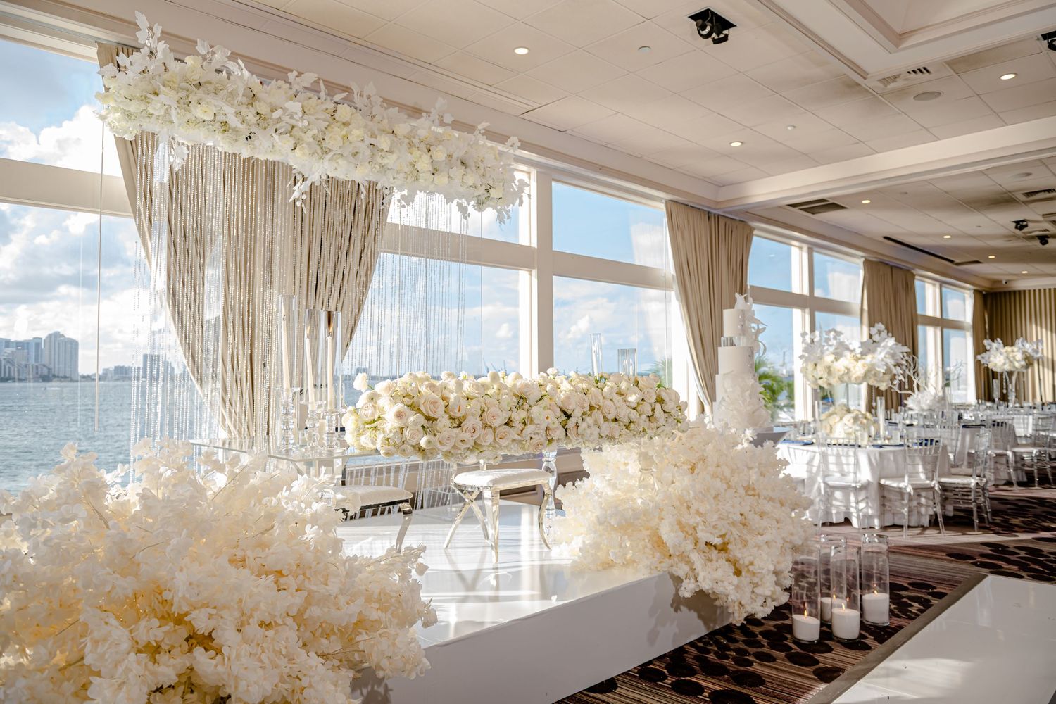 Luxurious white wedding reception venue with floral arrangements and waterfront views.