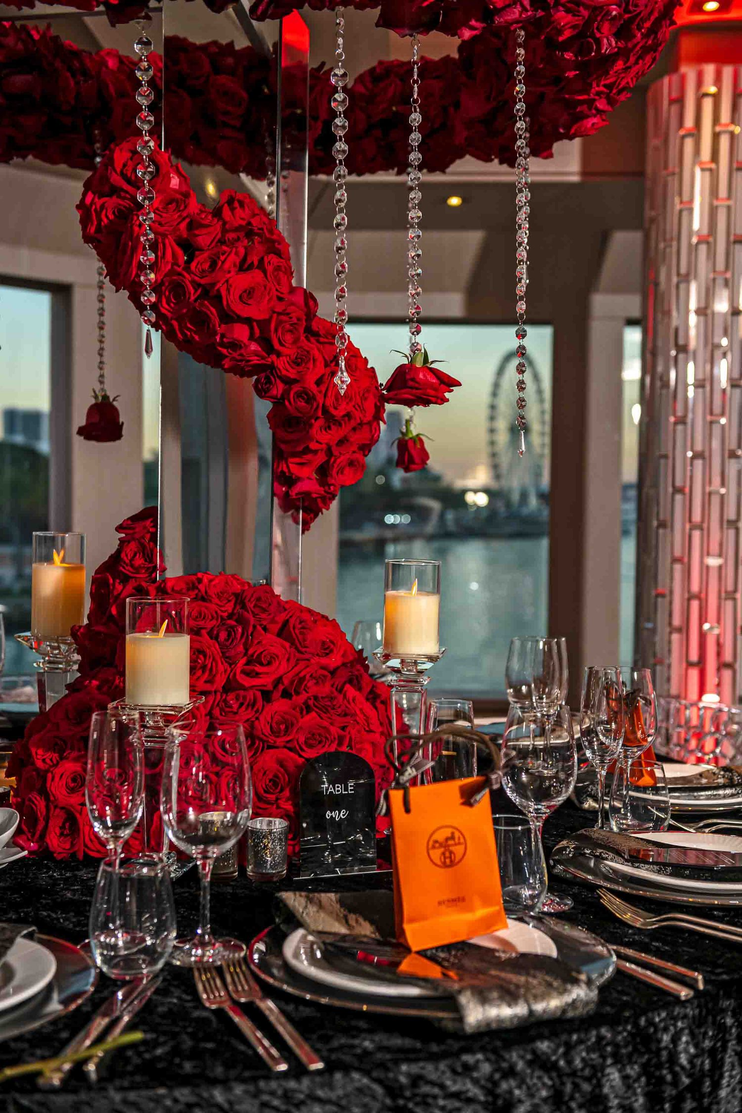 Elegant table setting with spiral red rose centerpiece, hanging crystals, and Hermes gift bags on the Seafair Mega Yacht in Miami.
