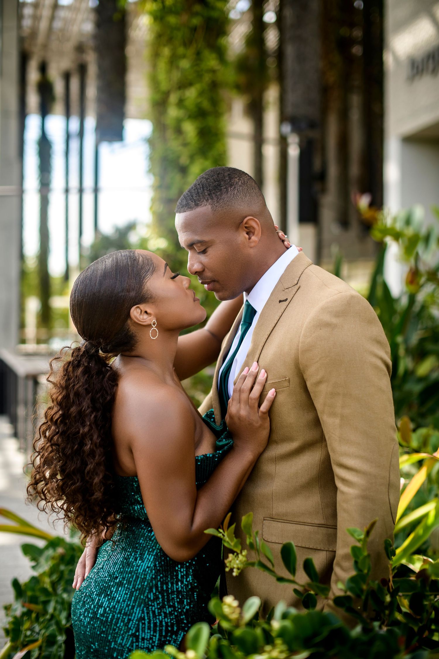 Intimate moment between couple in formal wear surrounded by lush garden foliage.