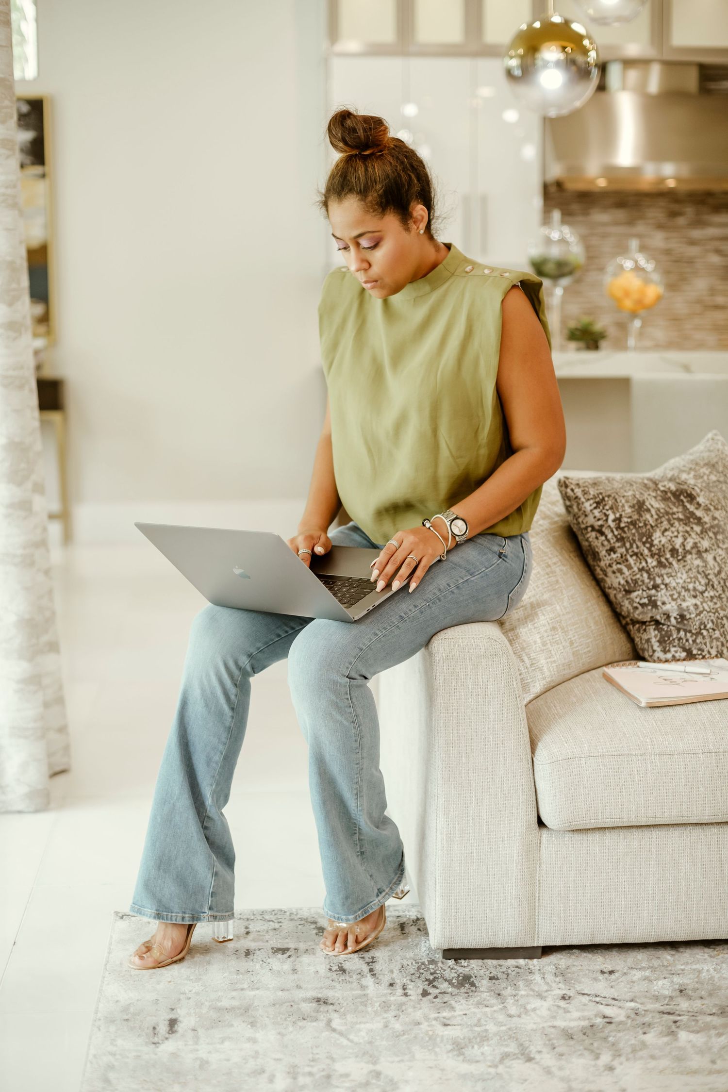 Woman in casual attire working on laptop while relaxing on couch at home.