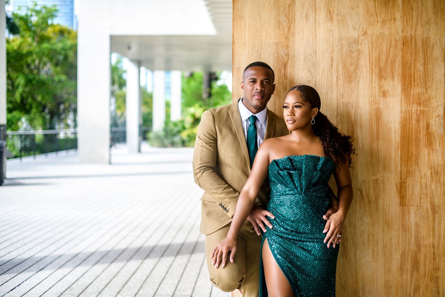 A couple in formal attire poses against a wooden wall in an elegant setting.