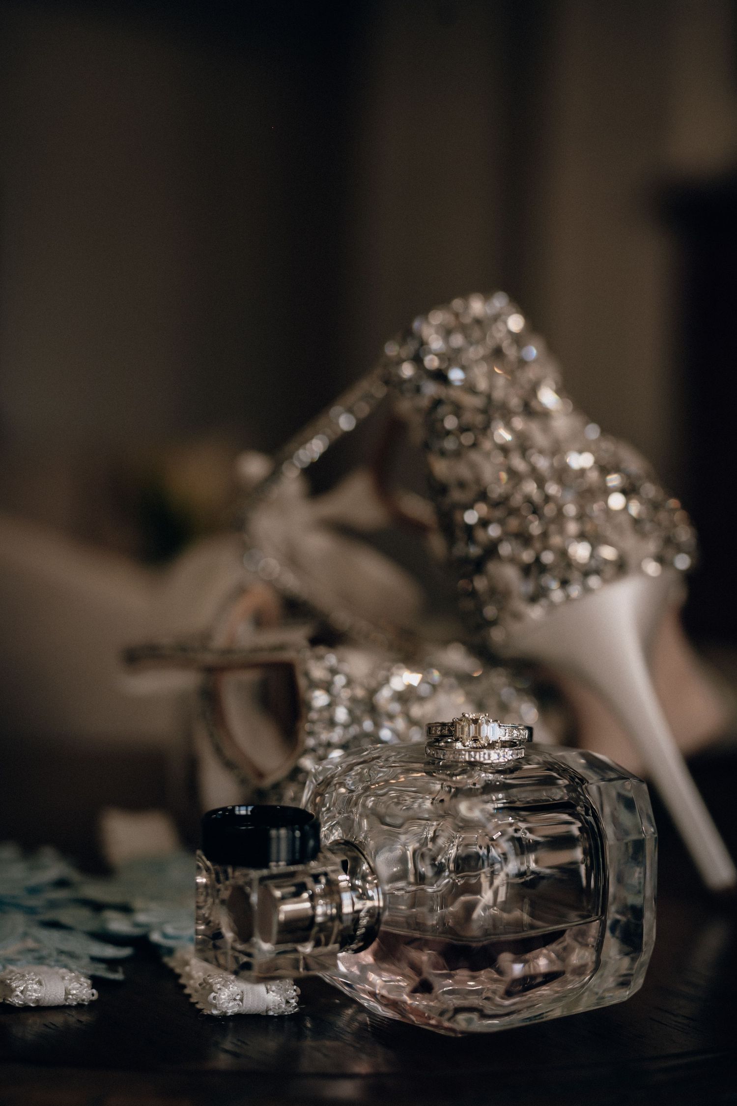 Elegant bridal accessories including sparkly heels and perfume bottles arranged on dark surface.