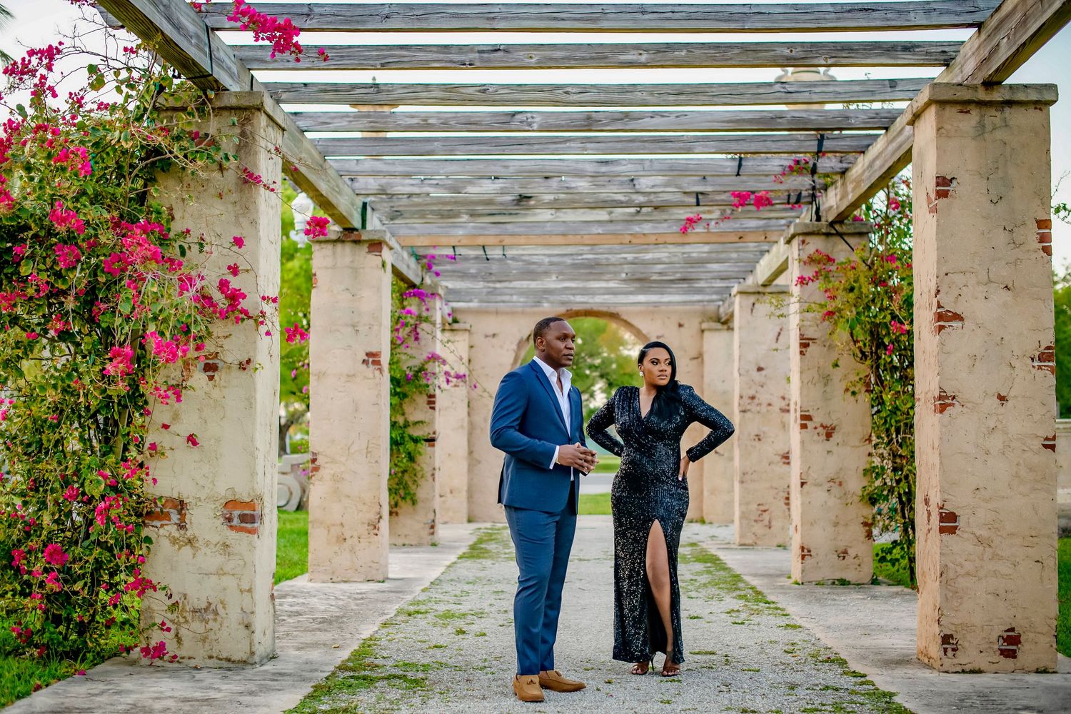 Covered walkway with climbing pink bougainvillea flowers and stone pillars creates a romantic garden setting.