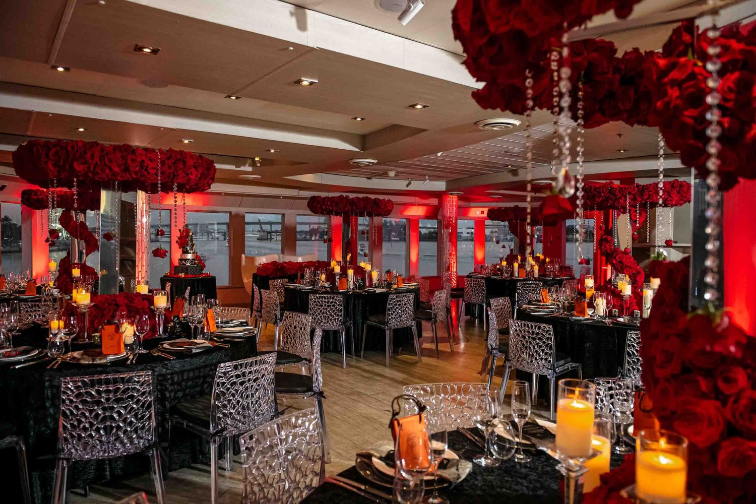 Modern event space with dramatic red floral arrangements and black table settings overlooking waterfront on the Seafair Mega Yacht in Miami.
