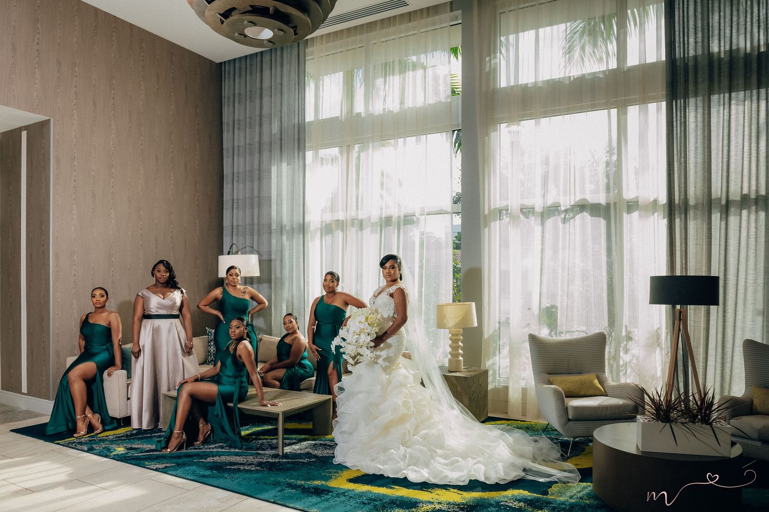 Wedding party relaxes in an elegant hotel room with floor-to-ceiling windows and modern decor.