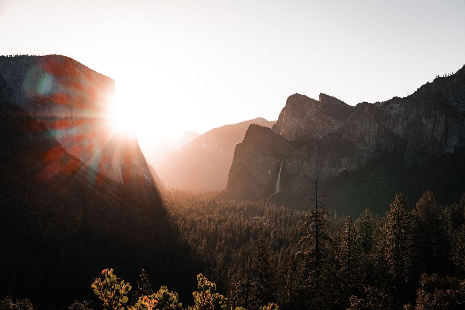 Dramatic sunrise view of Yosemite Valley with sunburst between mountain peaks.
