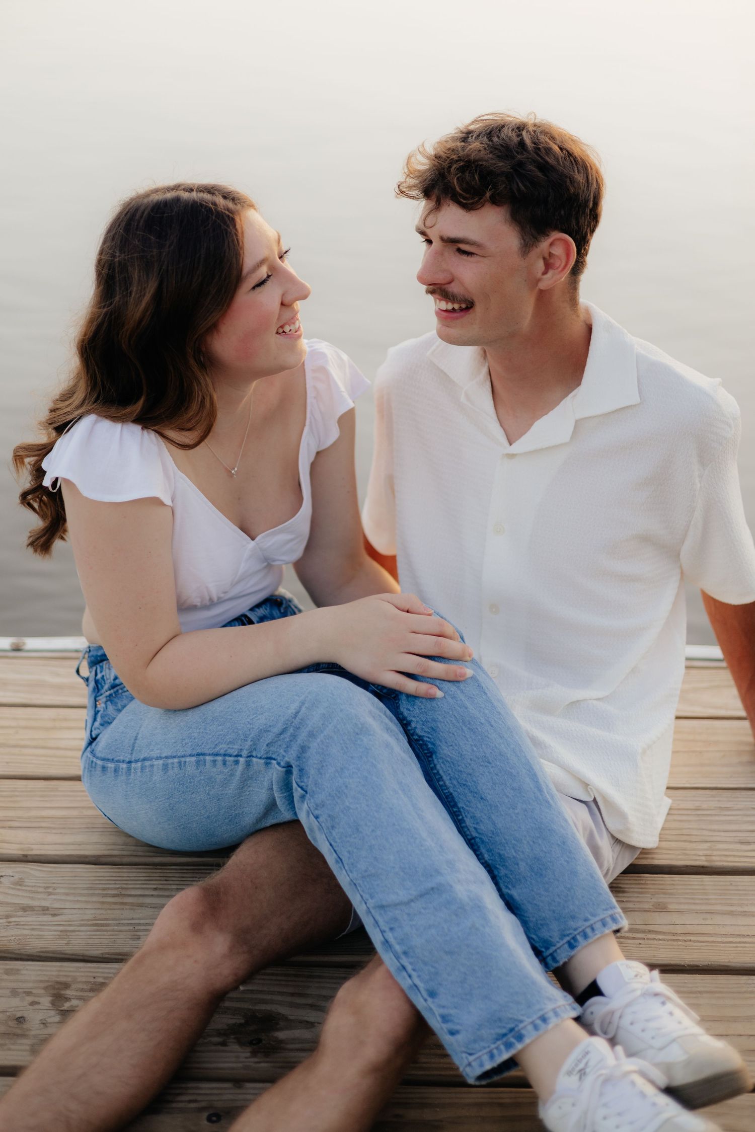 Couple smiling together along the lakeshore at Fish Lake Regional Park in Maple Grove, MN, with bright green trees, clear blue water