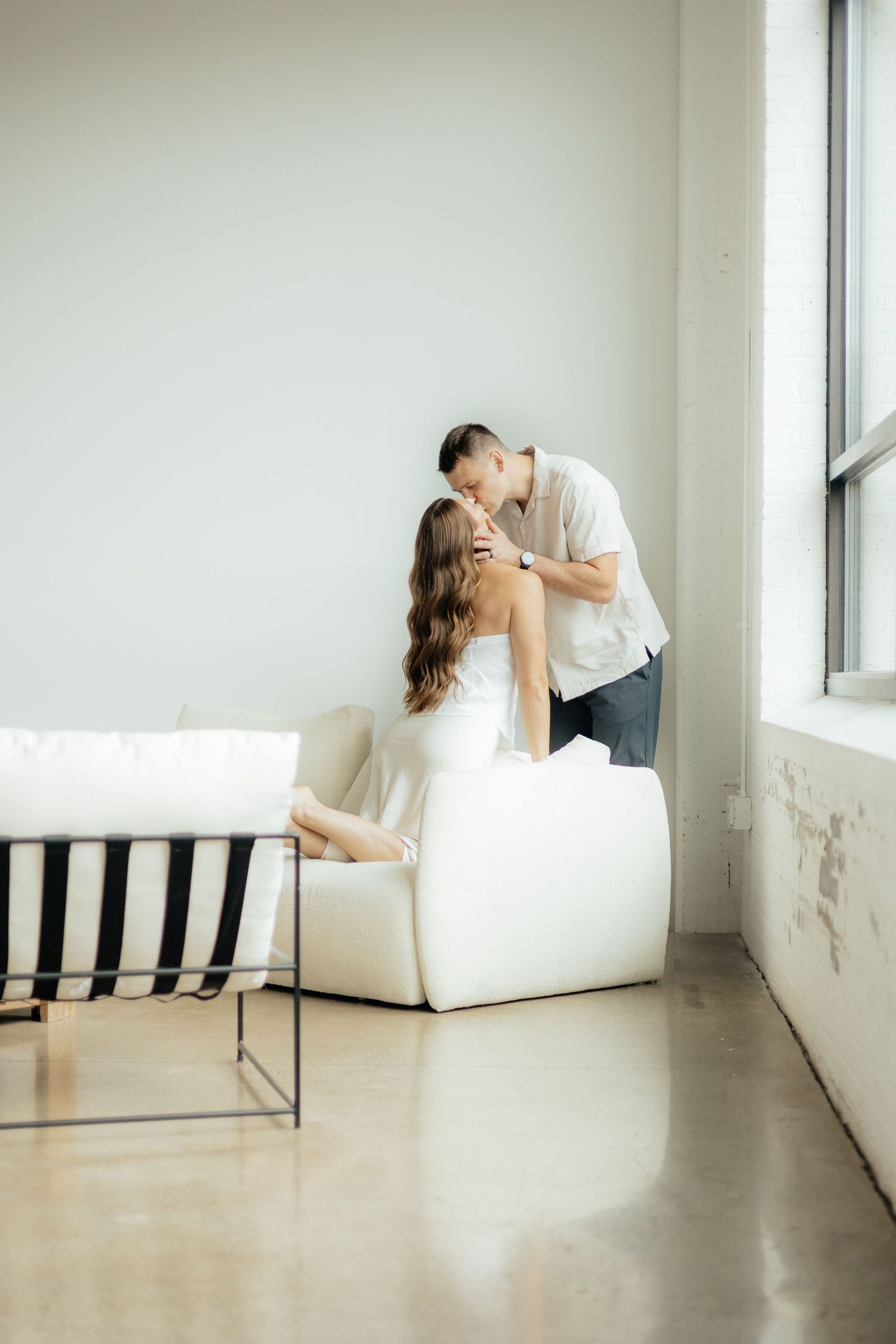 Couple embracing in soft natural light at Abide Studio in Minneapolis, MN, with minimalist white walls and warm, cozy tones