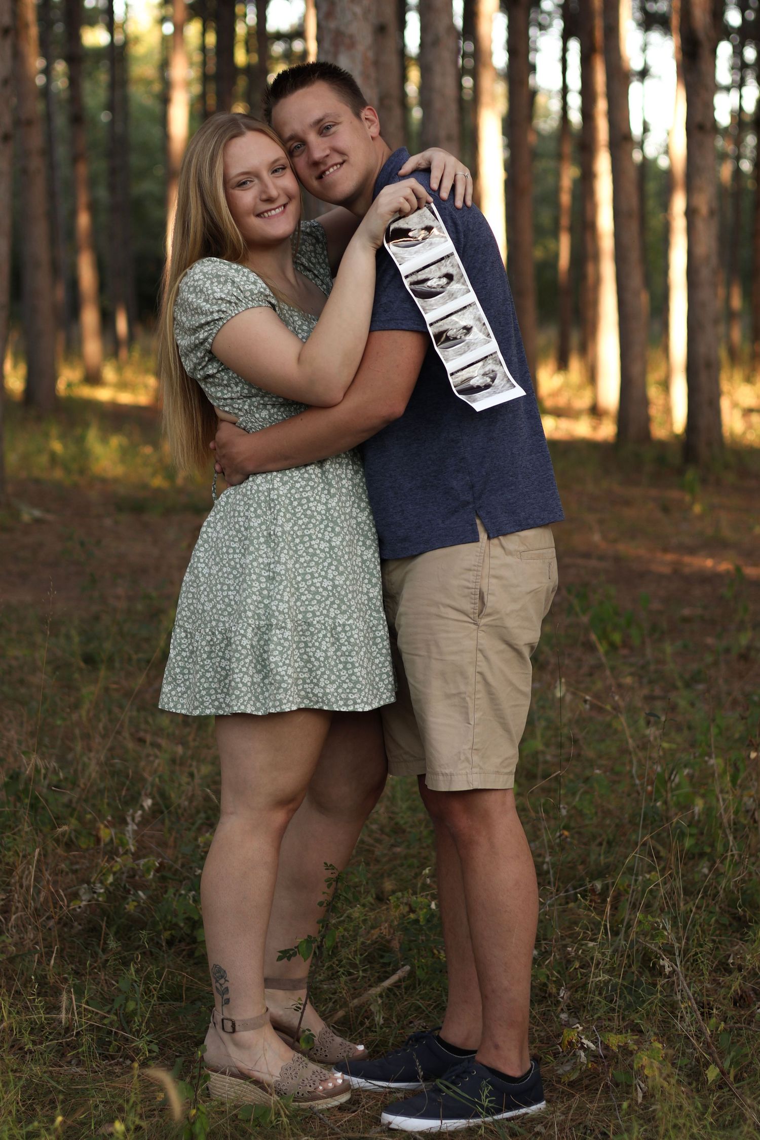 Expecting couple smiling and holding ultrasound photo near colorful fall foliage at Montissippi Park in Monticello, Minnesota
