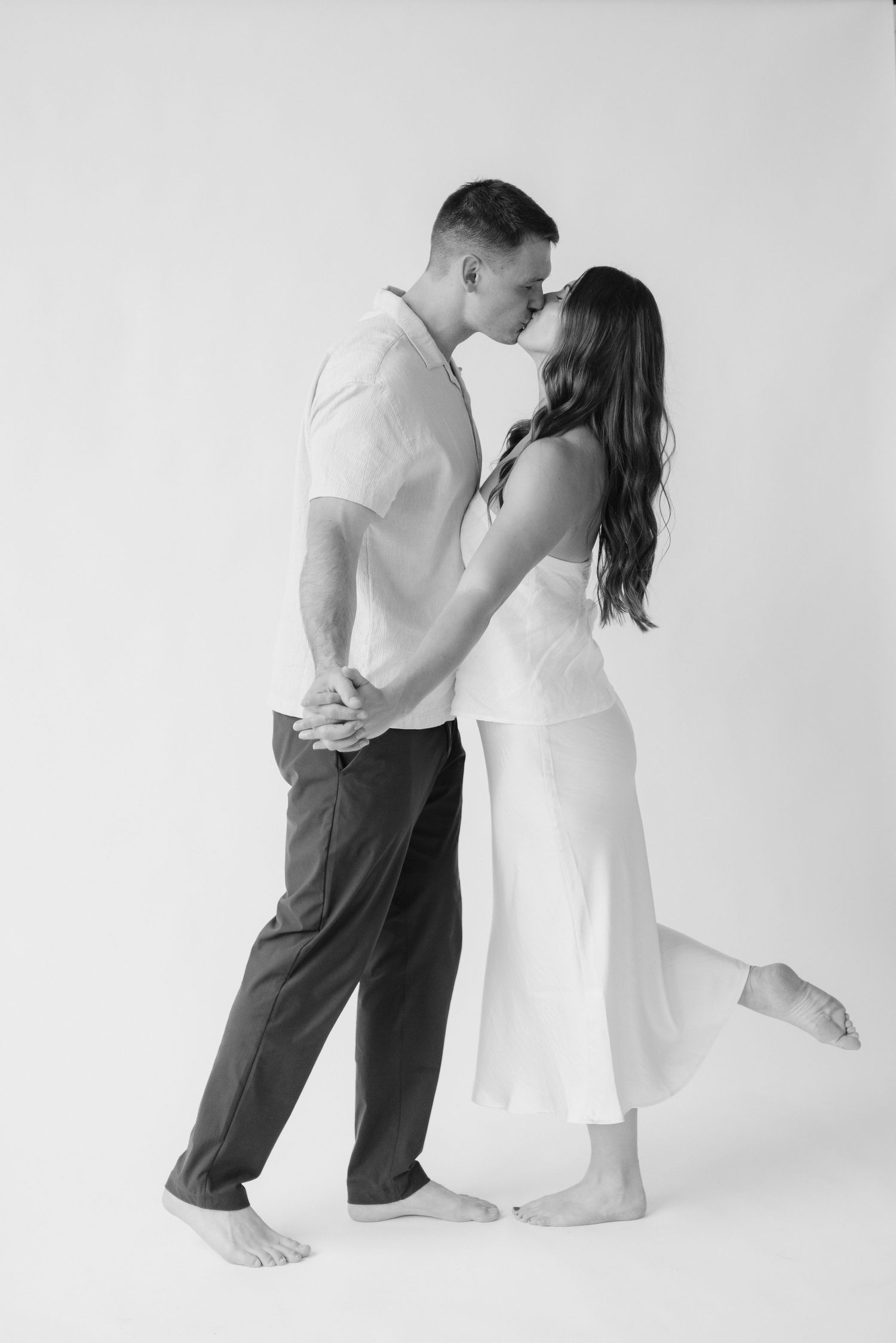 Couple embracing in soft natural light at Abide Studio in Minneapolis, MN, with minimalist white walls and warm, cozy tones