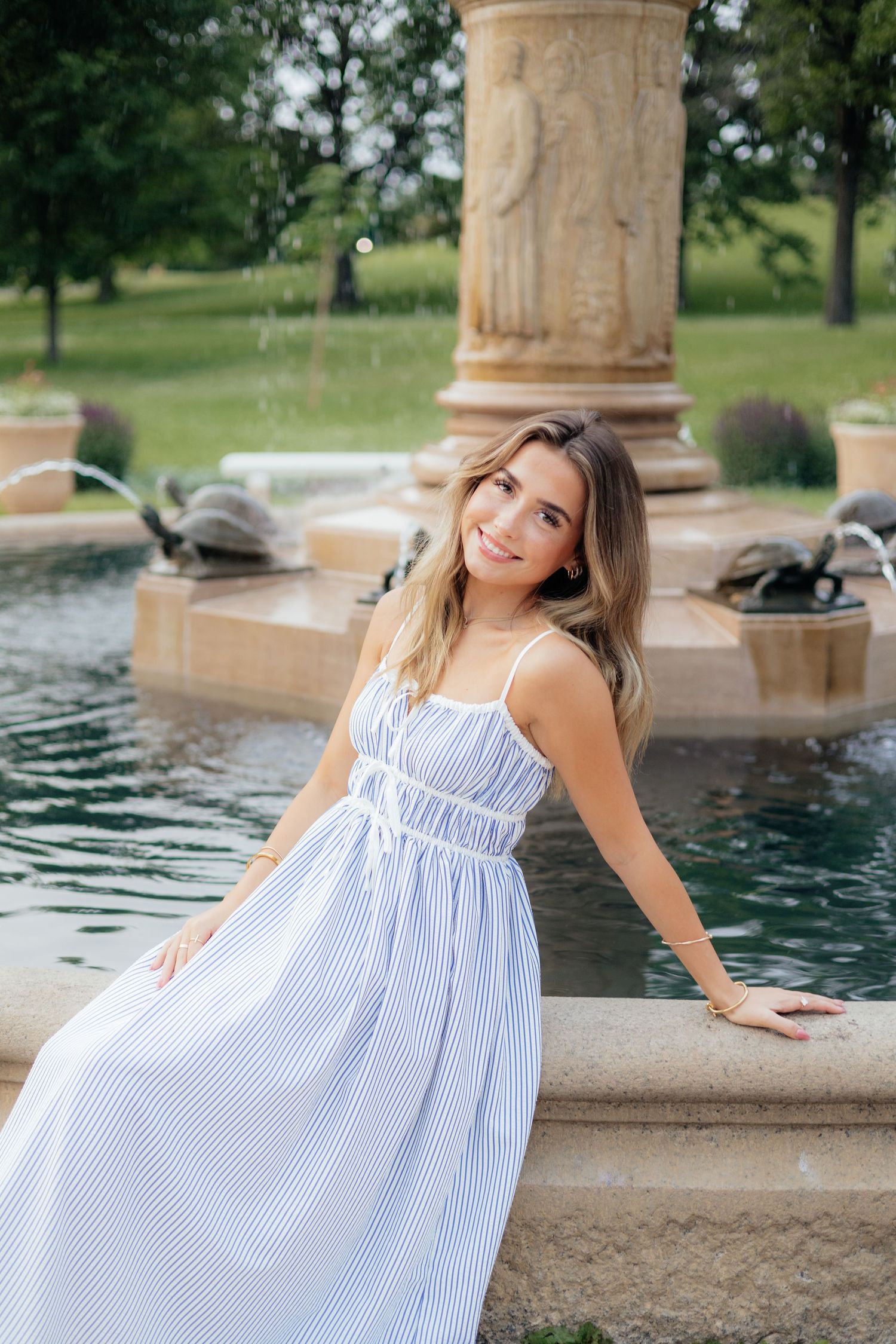 High school senior smiling and posing among blooming roses at Lyndale Park Rose Garden in Minneapolis, MN, surrounded by vibrant flowers and