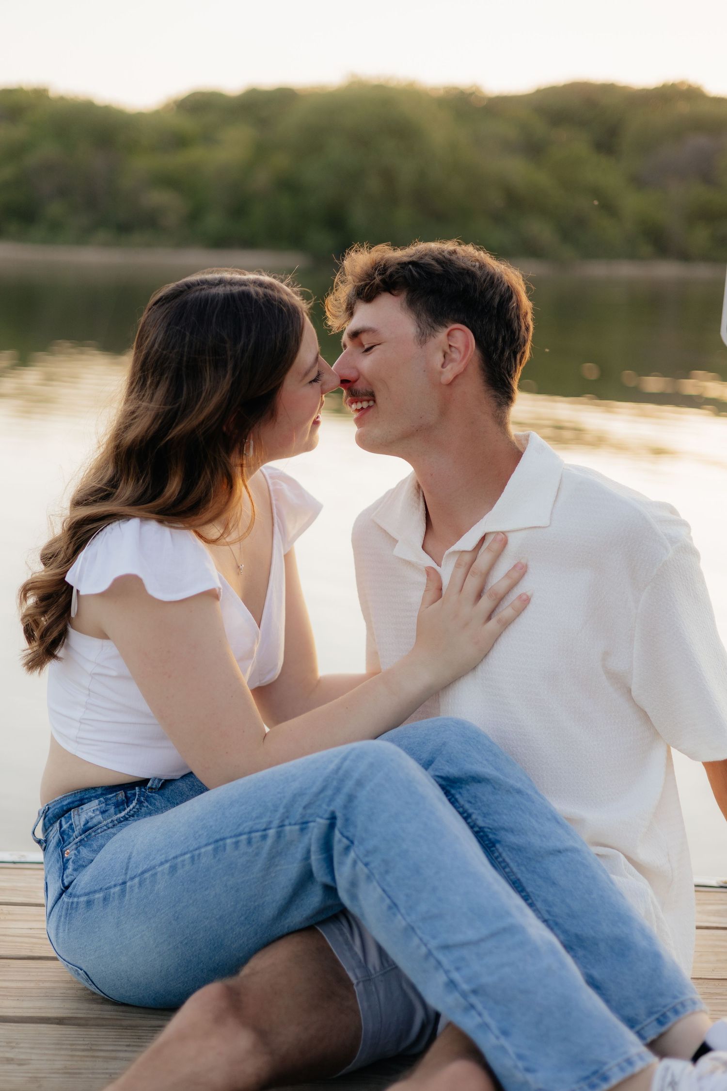 Couple smiling together along the lakeshore at Fish Lake Regional Park in Maple Grove, MN, with bright green trees, clear blue water