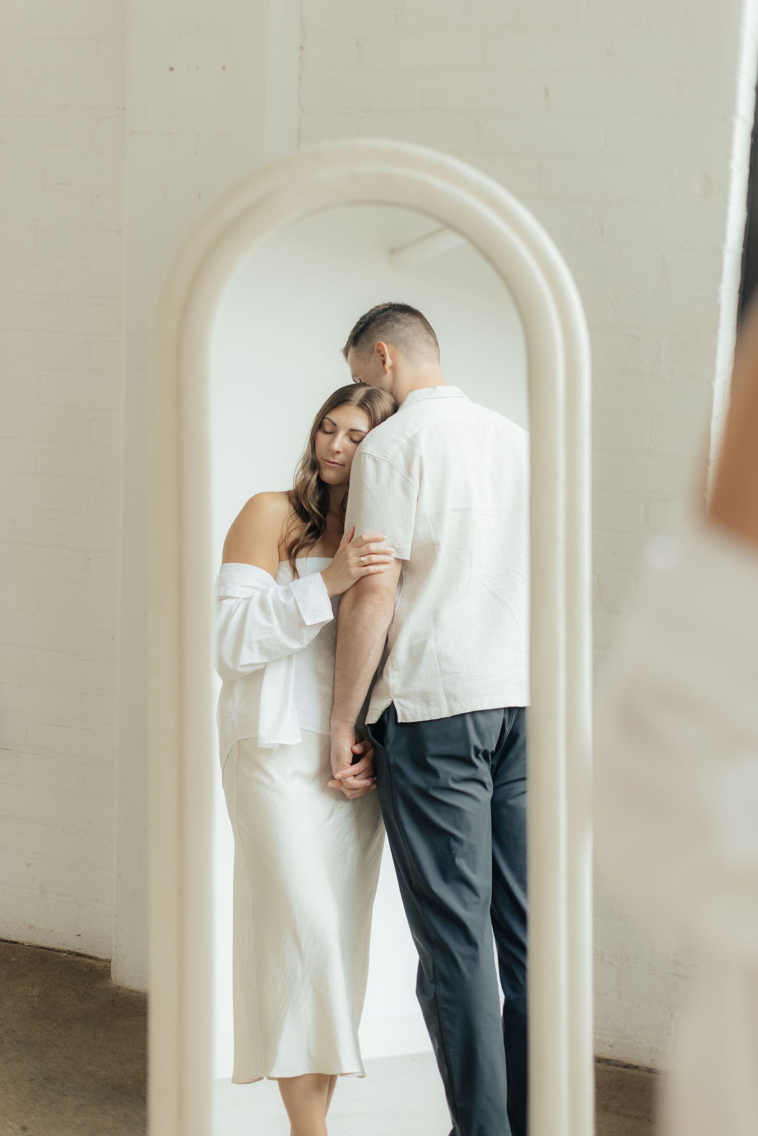 Couple embracing in soft natural light at Abide Studio in Minneapolis, MN, with minimalist white walls and warm, cozy tones