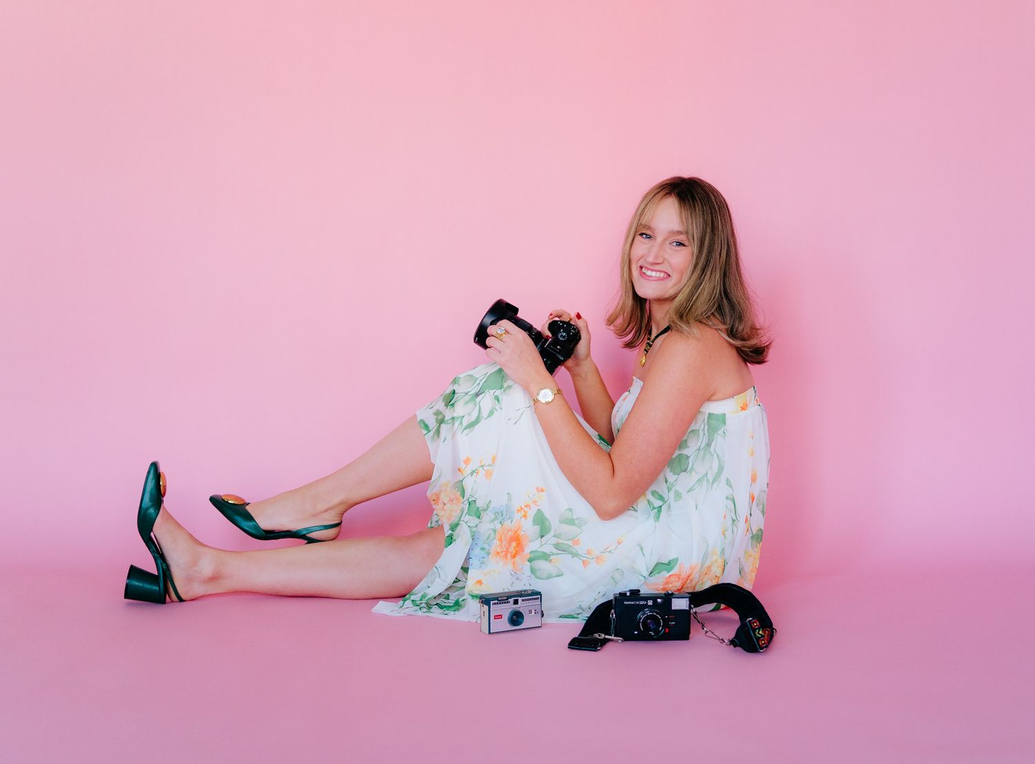 Person in vintage-style dress poses on pink background surrounded by retro black rotary telephones.