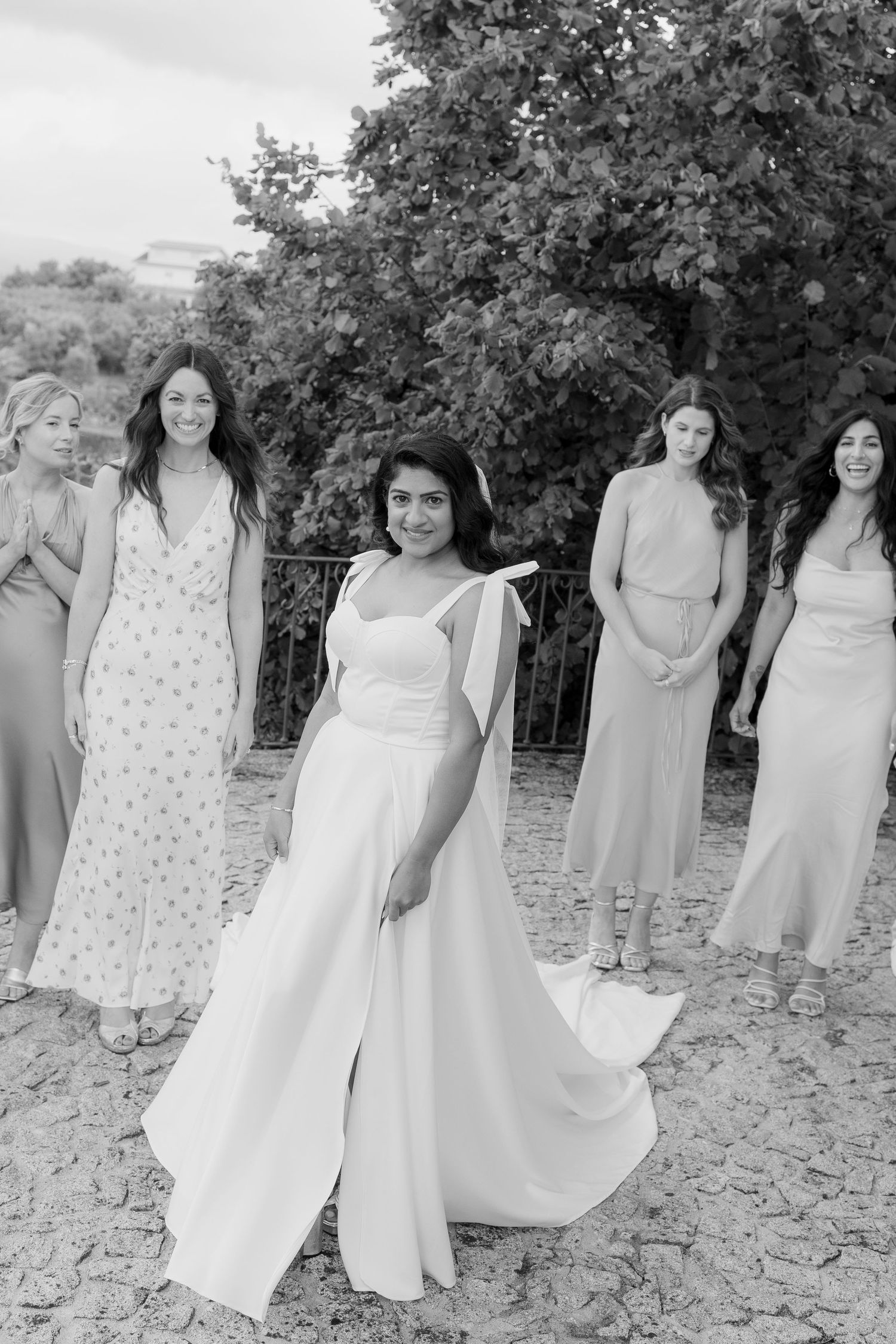 Bridal party in soft pastel dresses poses outdoors on a stone patio.