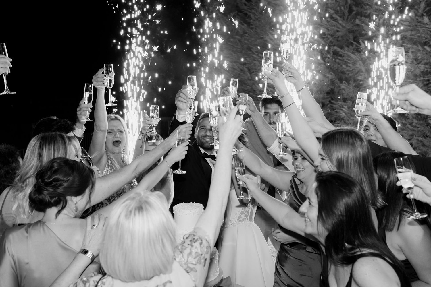 Wedding celebration at night with guests raising champagne glasses amid sparkling lights on the dance floor.