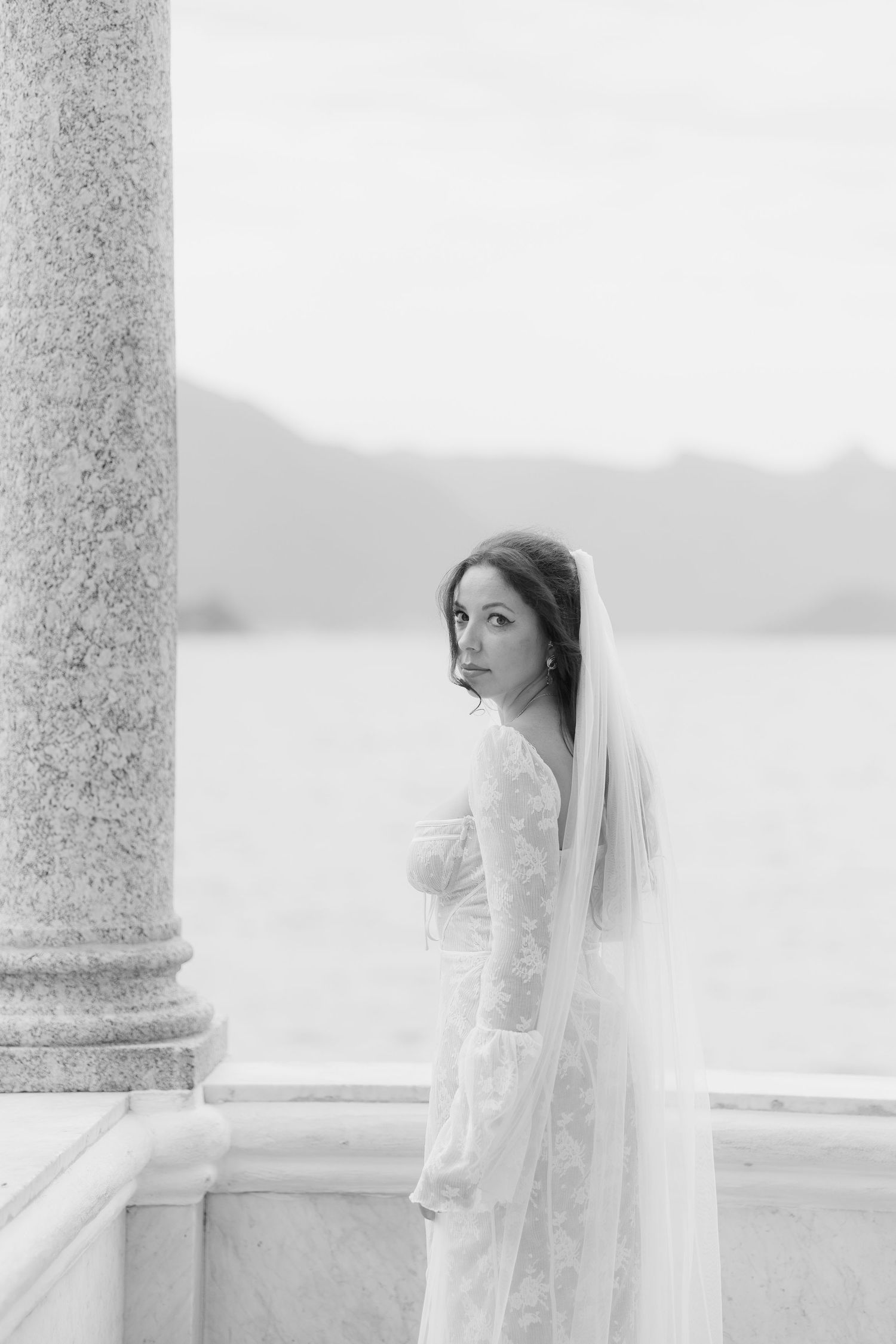 Black and white bridal portrait by a classical column overlooking a lake.