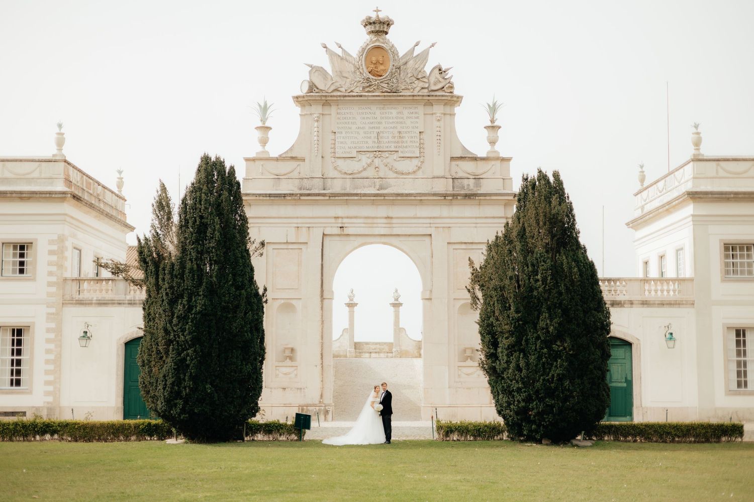 Distant silhouette of couple at grand white architectural entrance with cypress trees.