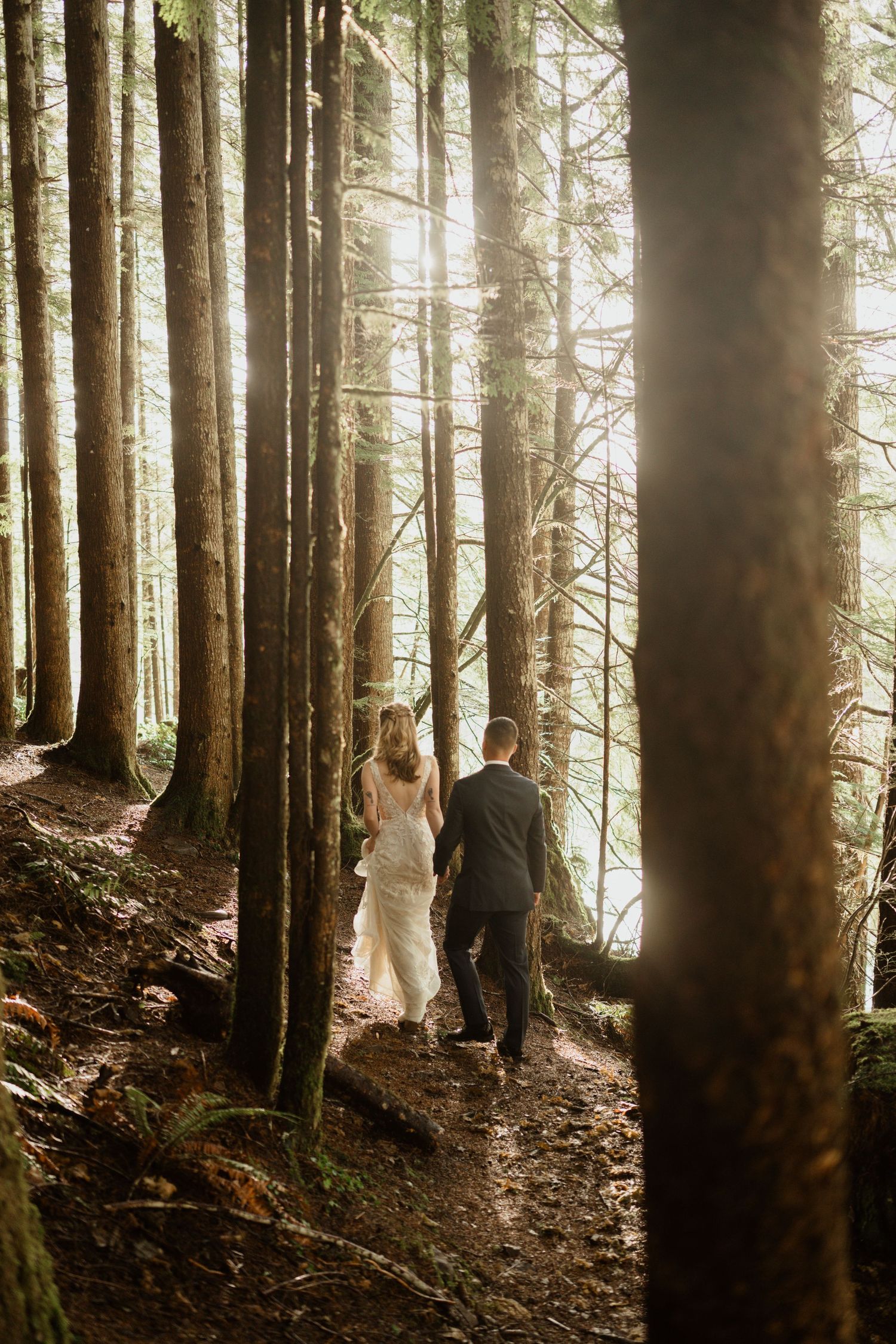 A couple walks through a misty forest path surrounded by tall evergreen trees.
