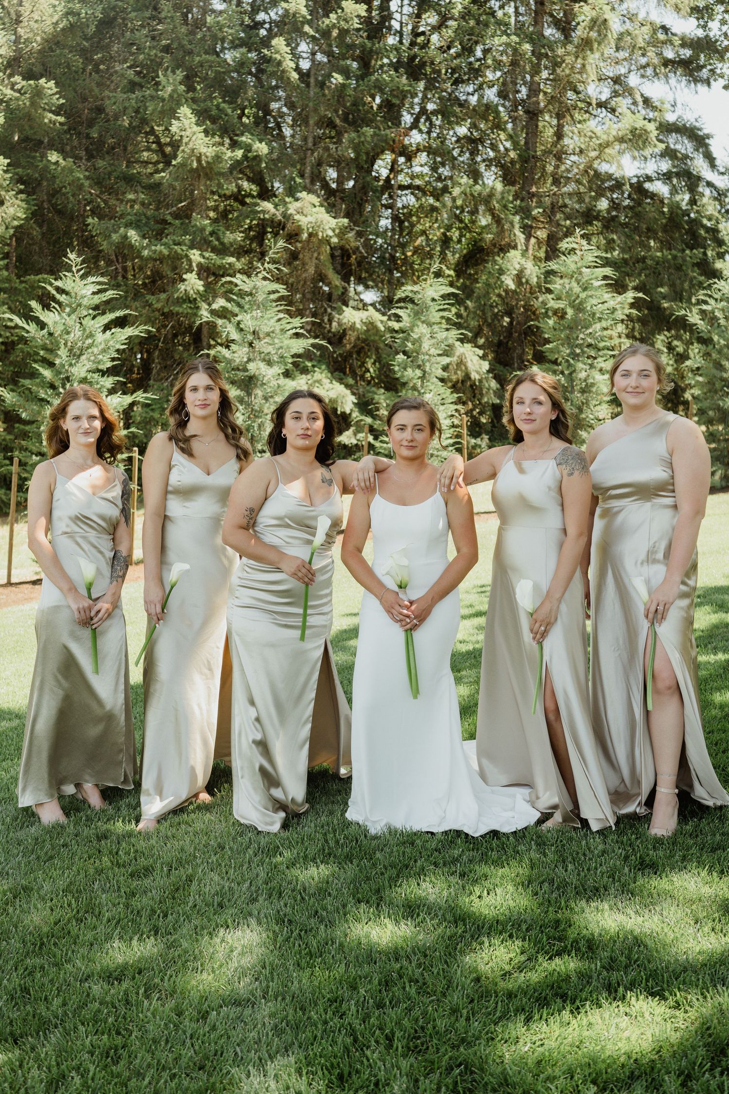 Bridal party in coordinating champagne and white dresses pose on green lawn.