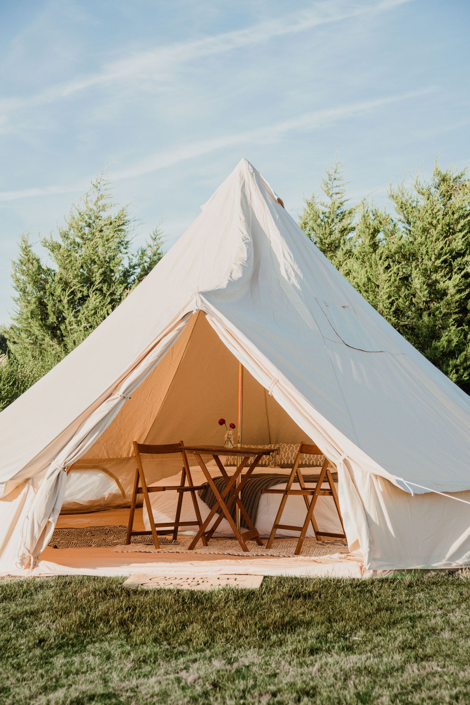 A white bell tent set up on grass with folding chairs visible inside.