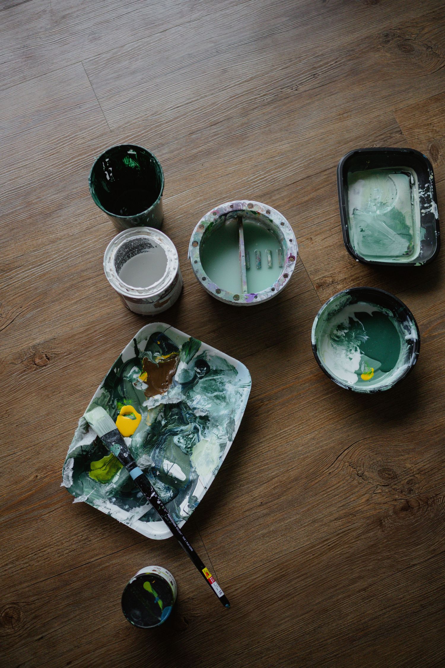 Various containers of green paint and art supplies arranged on wooden flooring.