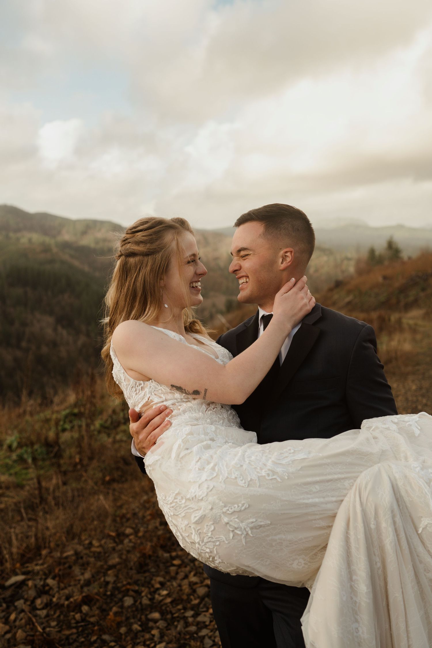 A groom carries his bride in a playful moment on a scenic mountainside.