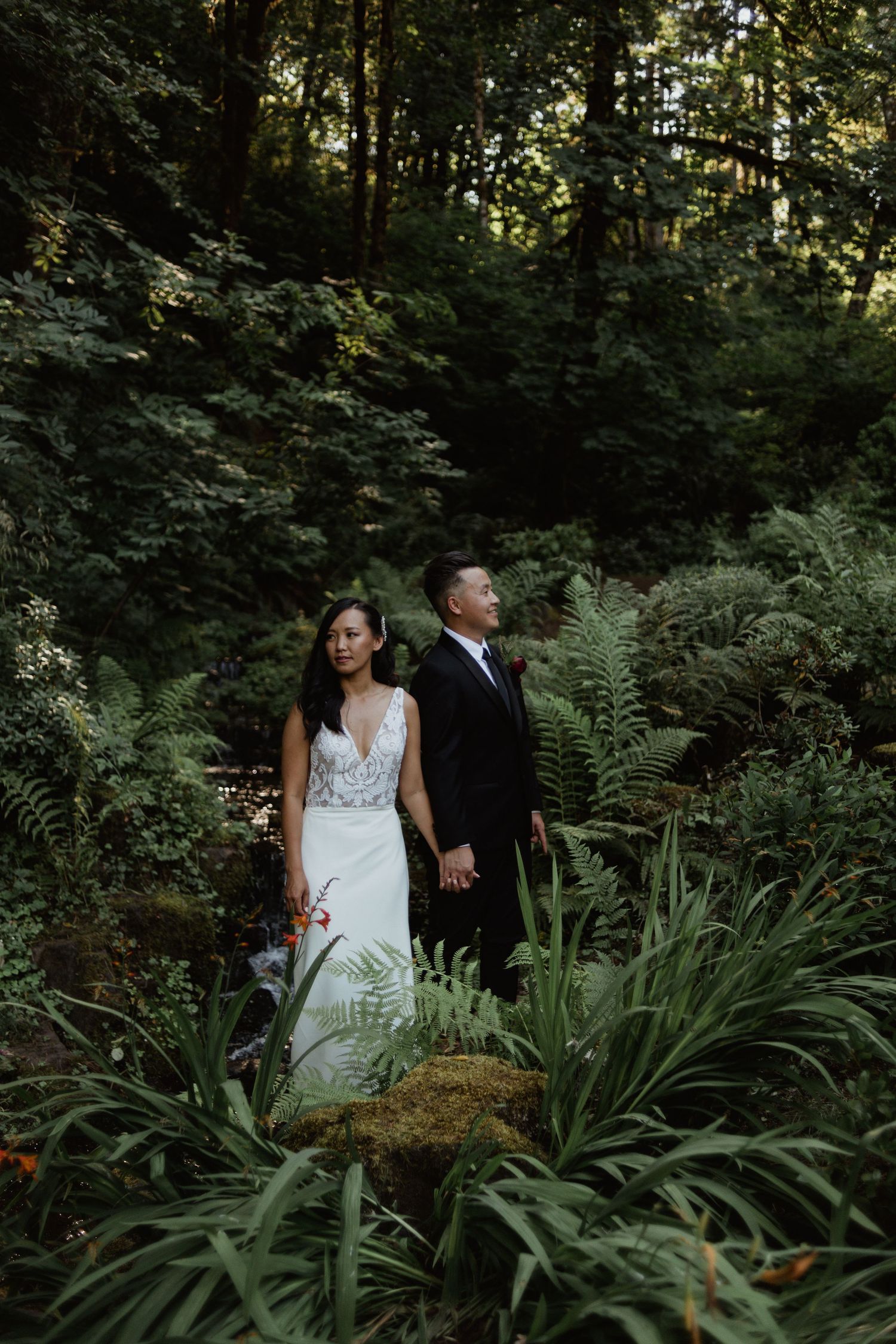 Wedding couple standing in a lush forest garden surrounded by ferns and greenery.