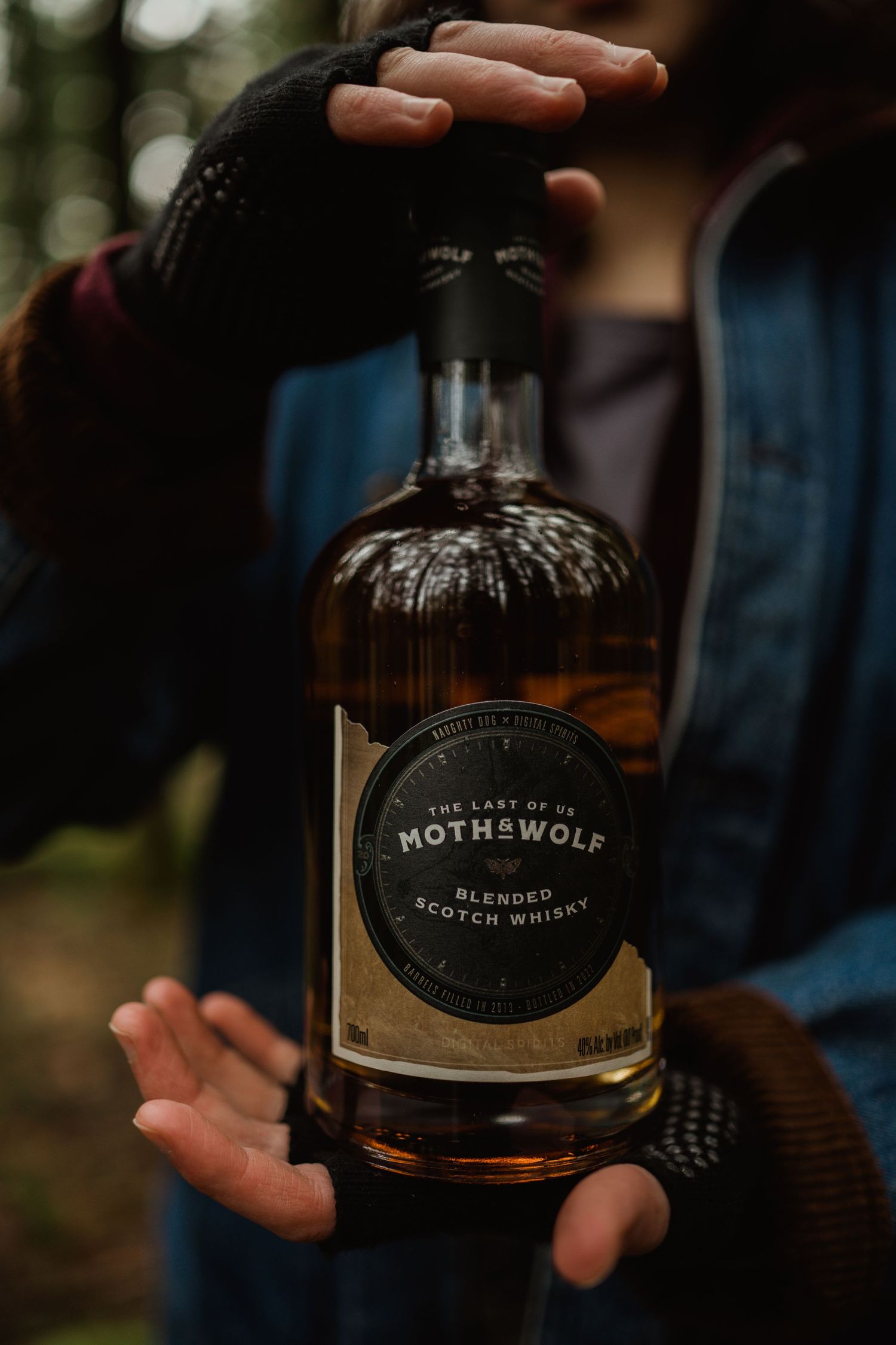 A bottle of Moth & Wolf craft whiskey held in hands against a blurred background.