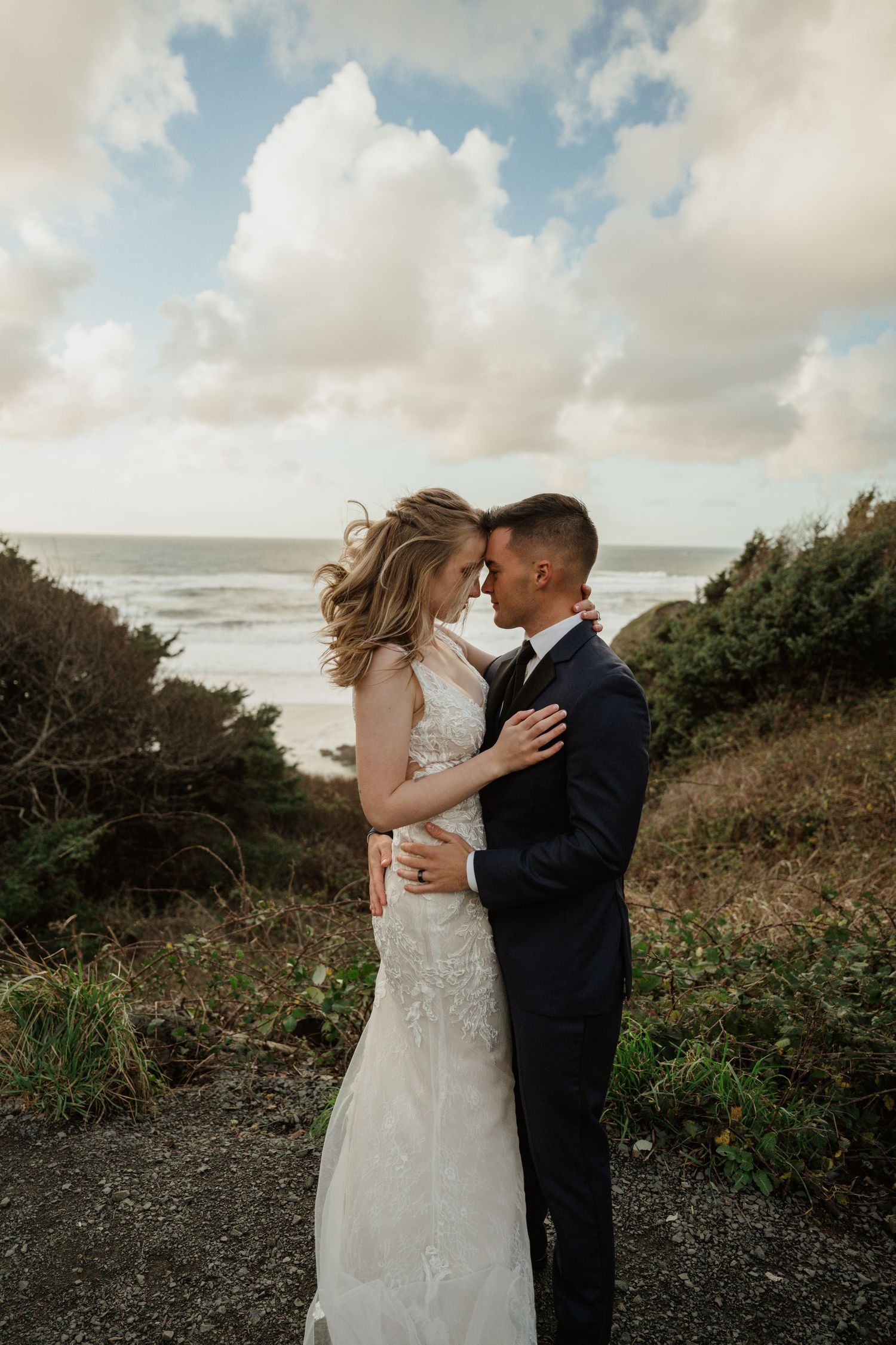 A romantic embrace on a coastal cliff with cloudy skies and ocean views.
