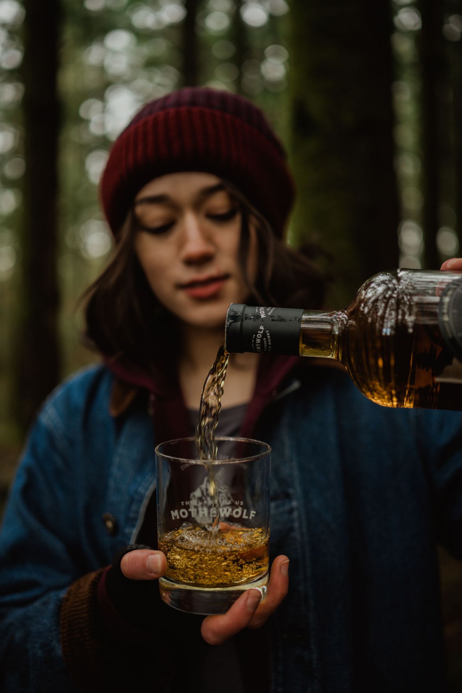Whiskey being poured into a branded glass in an outdoor forest setting.