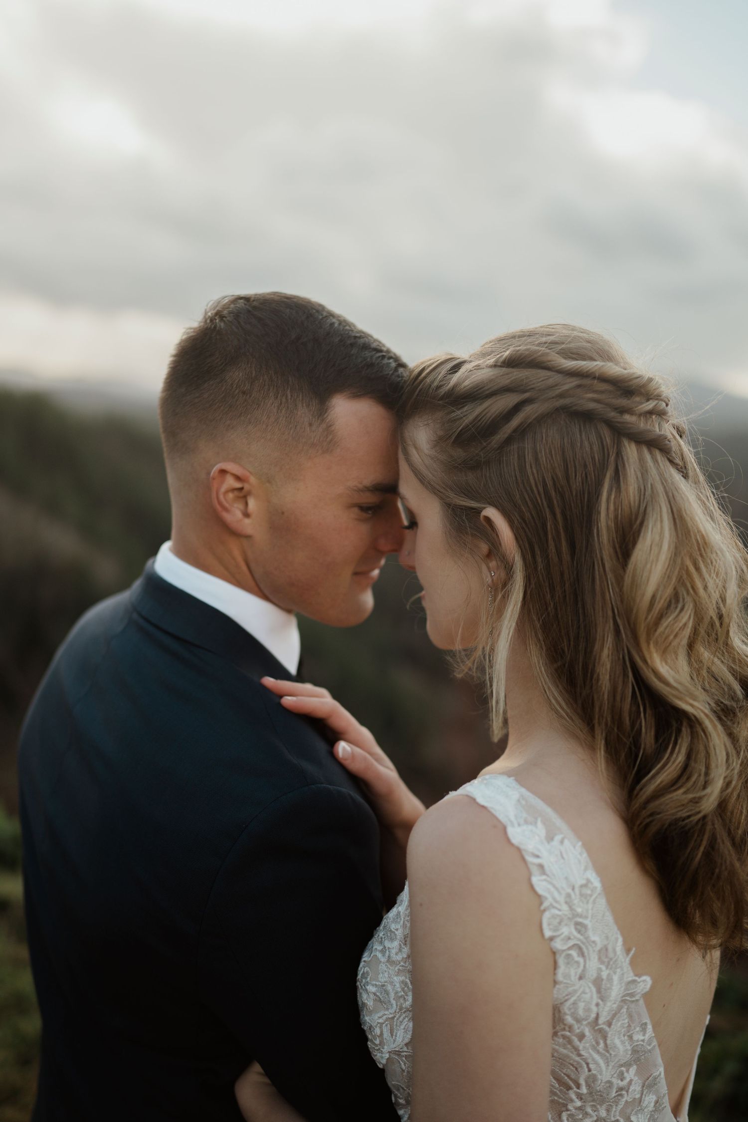 An intimate moment between newlyweds against a cloudy mountain backdrop.